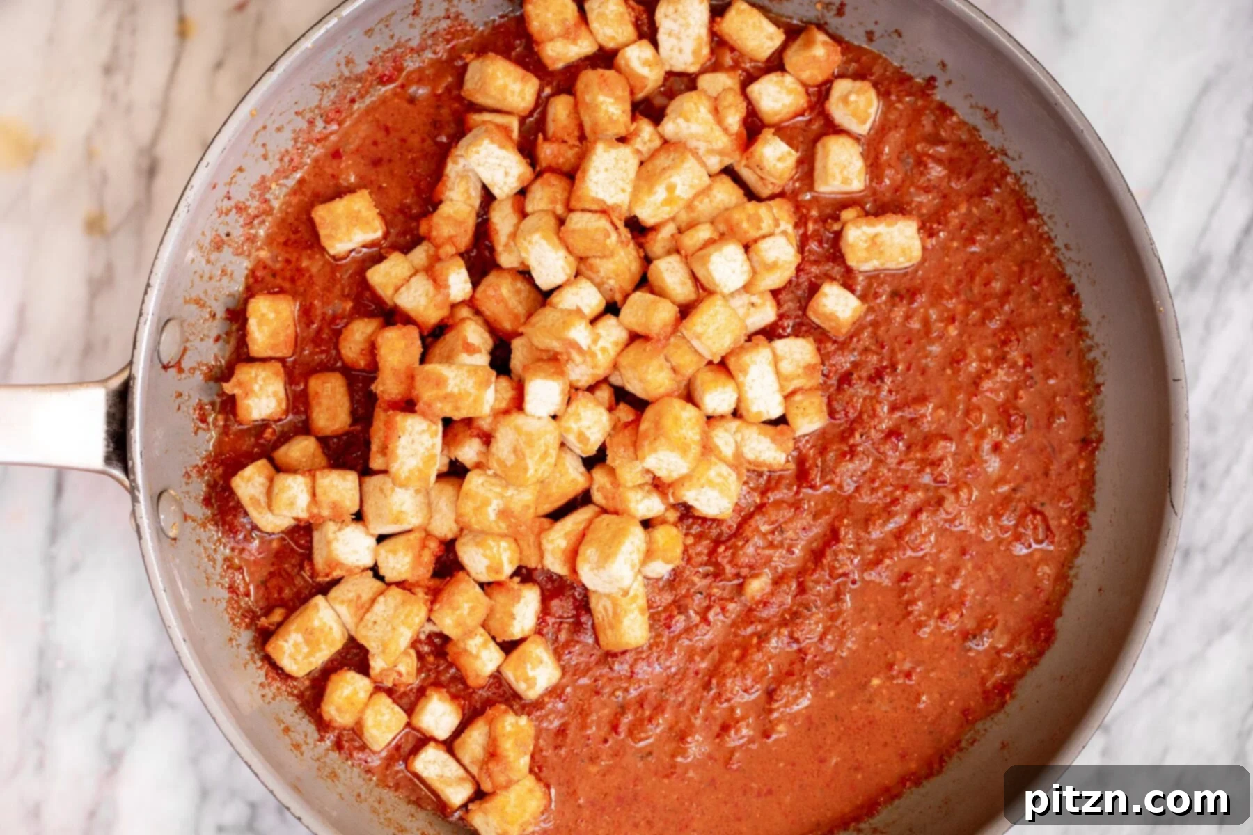 Pan-fried tofu cubes being gently added to the simmering chili gravy in a sauteing pan, ready to absorb the rich flavors.