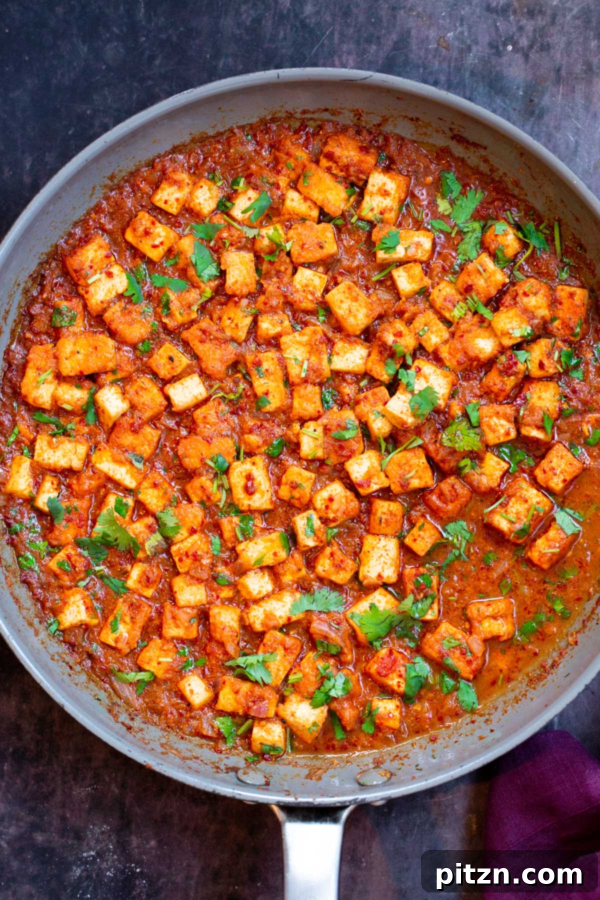Close-up of Tofu Vindaloo curry simmering in a grey skillet, showcasing its rich texture and color.