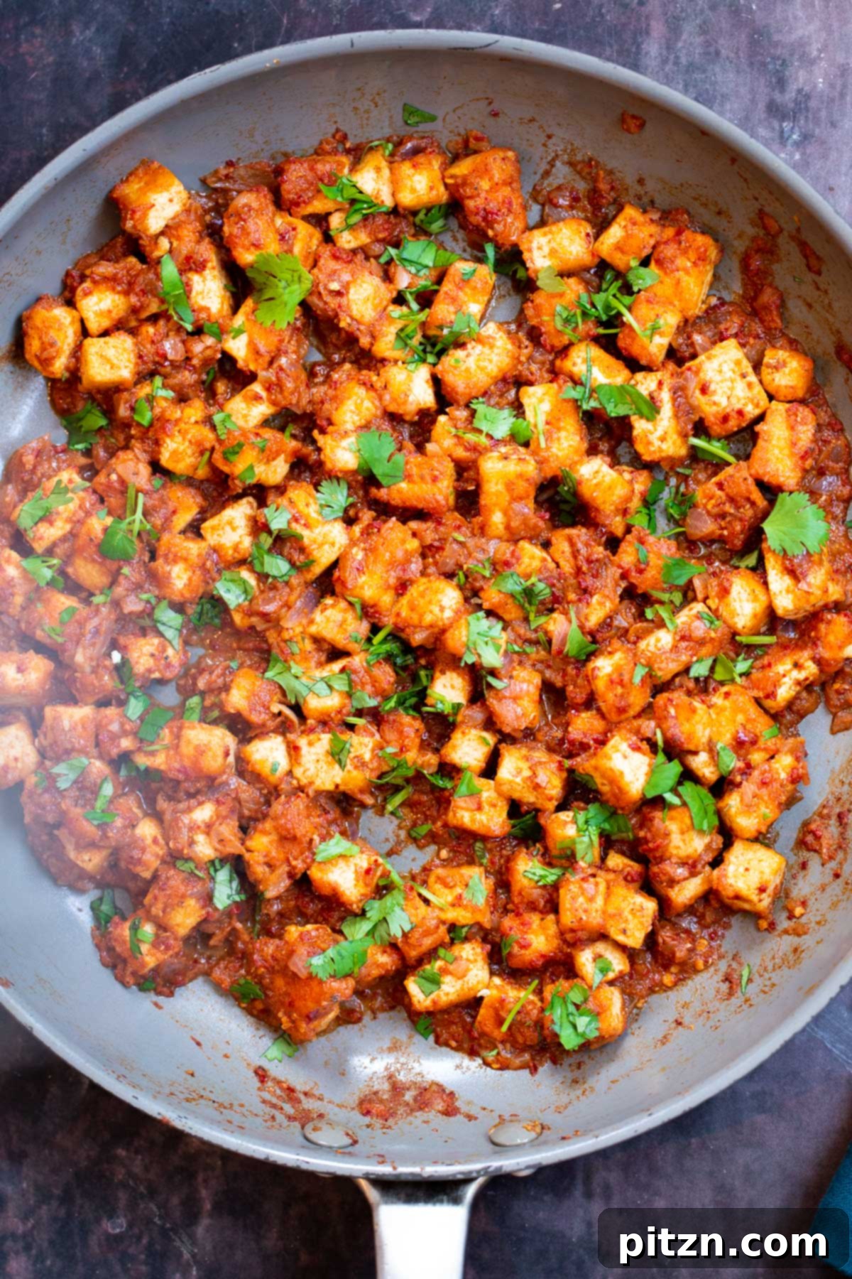 Tofu Vindaloo curry beautifully plated in a sauteing pan, highlighting its rich texture and color, garnished with fresh herbs.