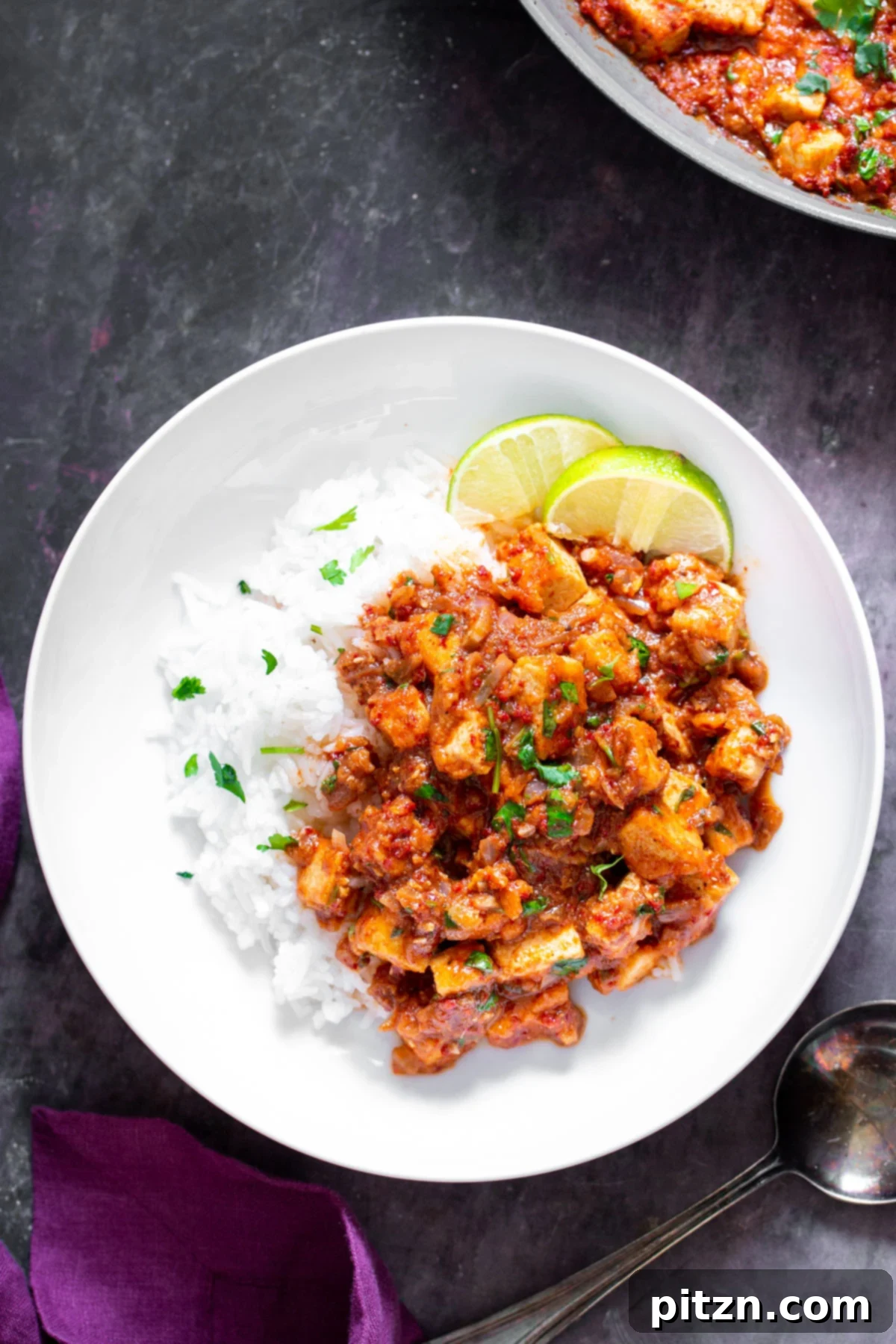 Tofu Vindaloo curry elegantly presented on a white plate with steamed rice and fresh lime slices for garnish.