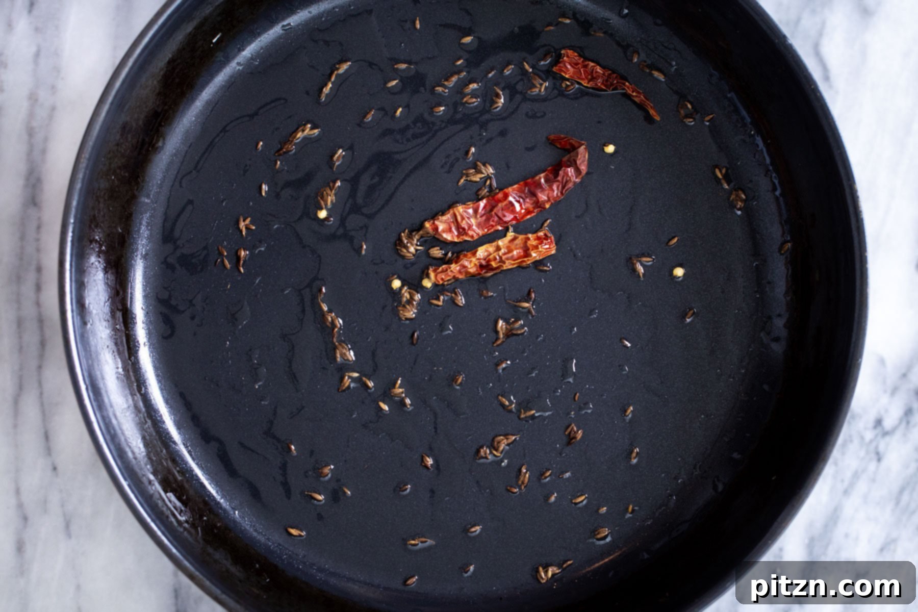 Cumin seeds and dried red chilies frying in oil, creating a fragrant foundation for the Indian curry.