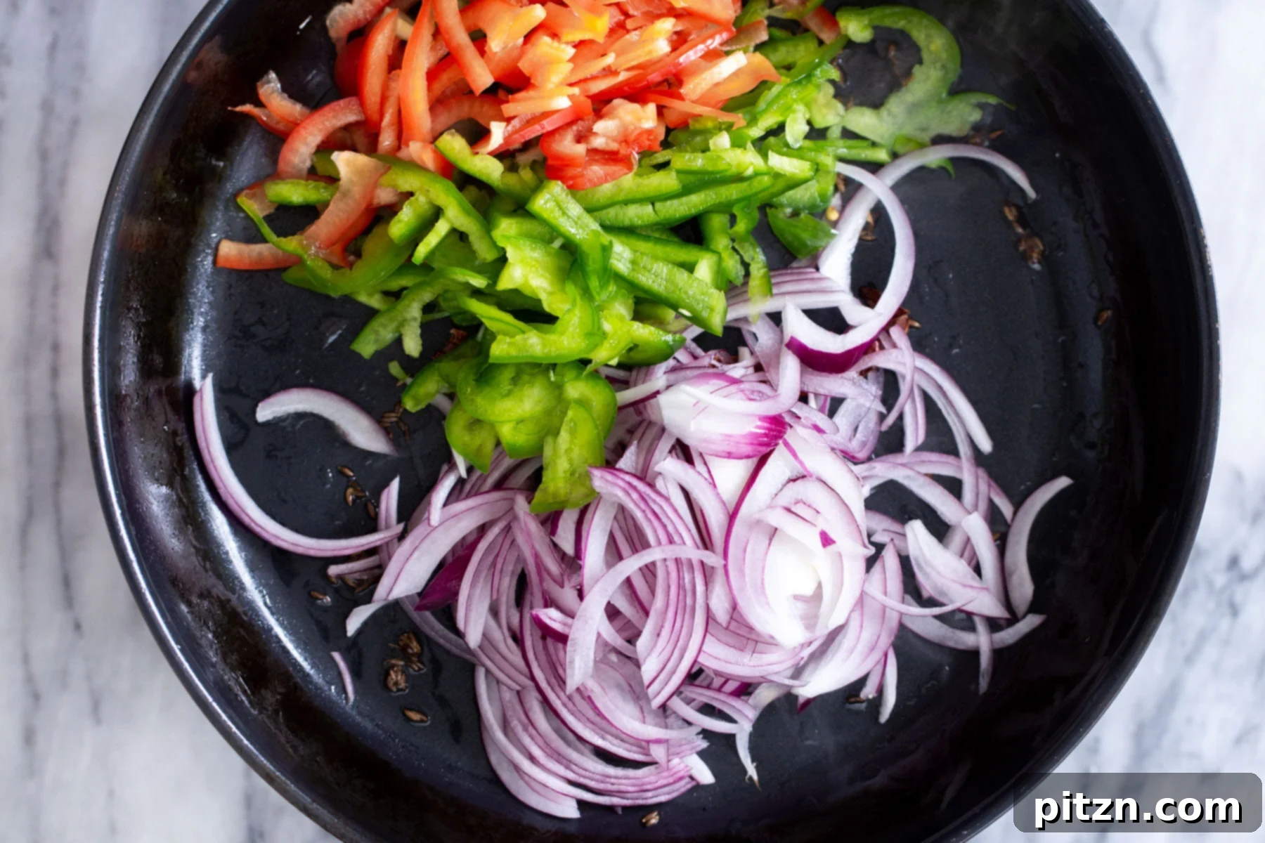 Sliced bell peppers and onions being added to a hot skillet with tempered spices for the Jalfrezi base.