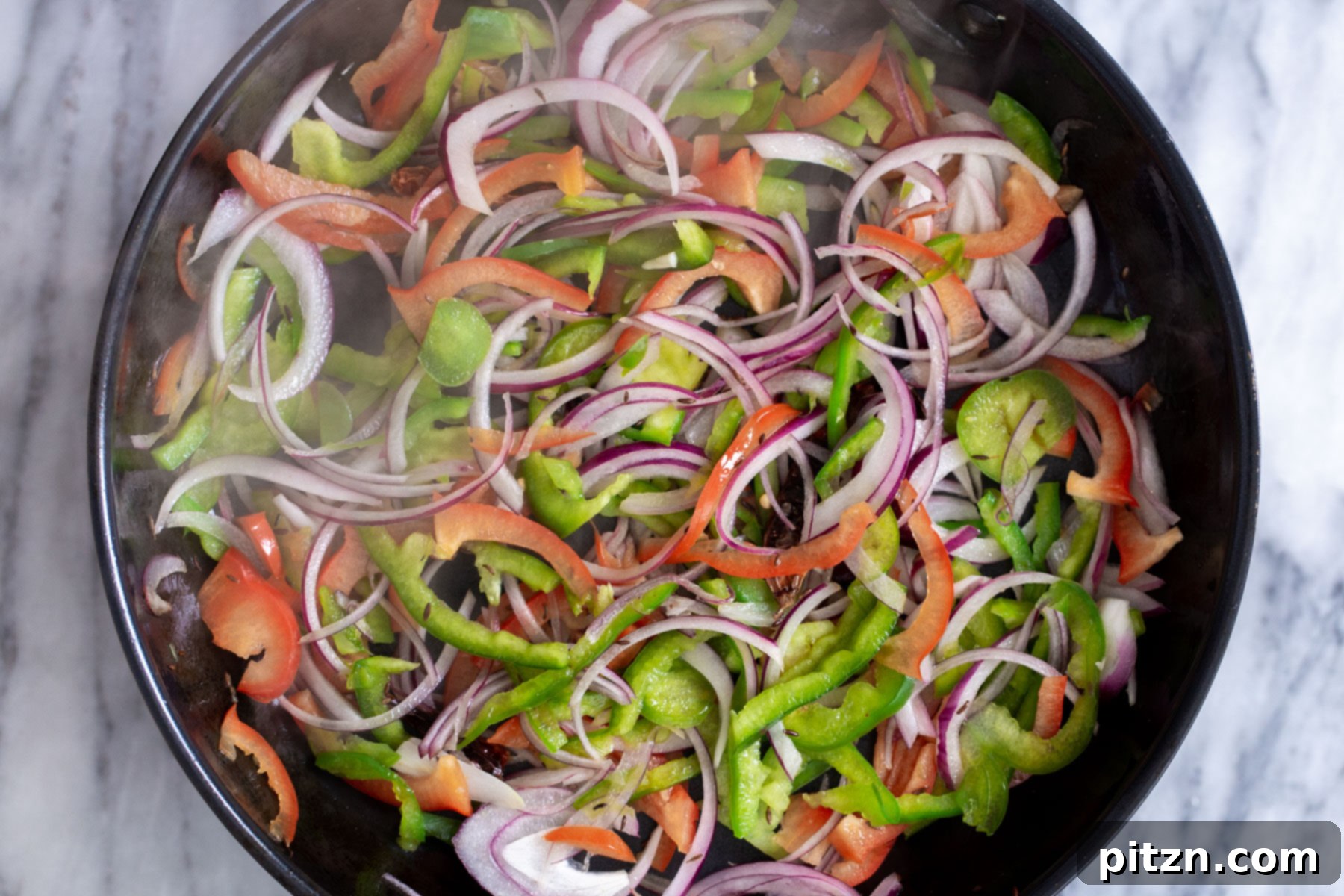 Sautéed bell peppers and onions in a skillet, cooking down to develop sweetness and char.