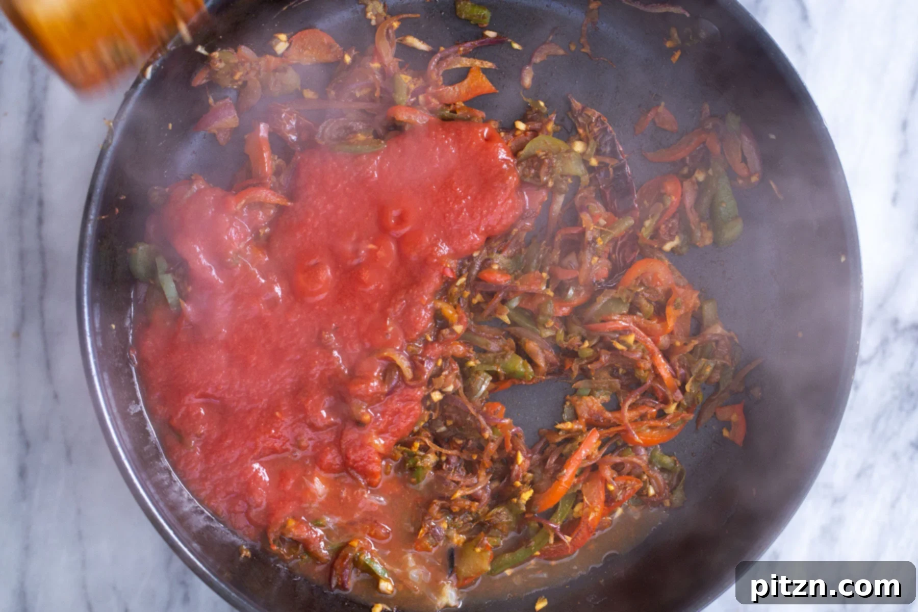 Rich tomato sauce being added to a skillet containing sautéed bell peppers and aromatic spices, forming the Jalfrezi gravy.