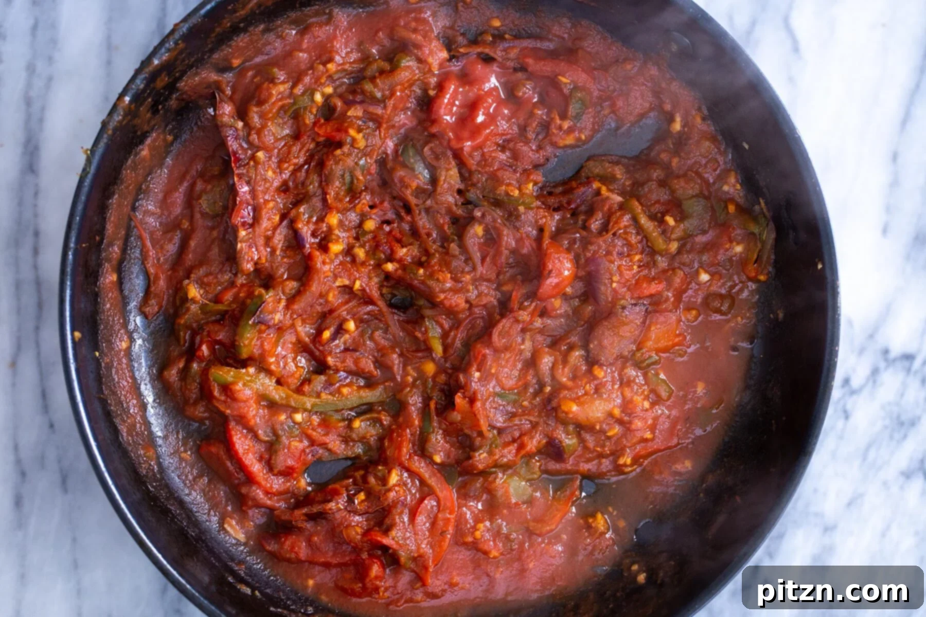 The vibrant Jalfrezi sauce simmering in a skillet, rich with tomatoes, peppers, and spices.