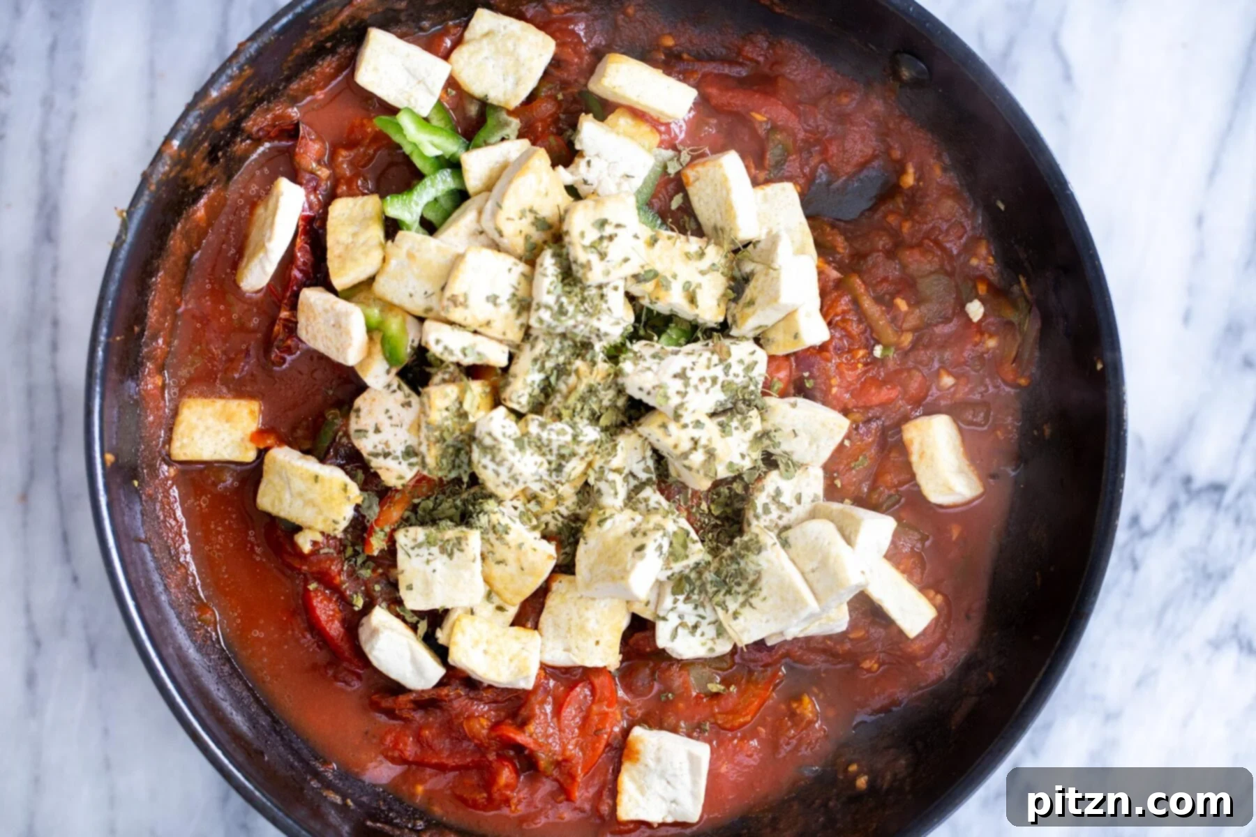 A black skillet filled with rich tomato gravy and golden-fried tofu cubes, generously seasoned with fenugreek leaves.