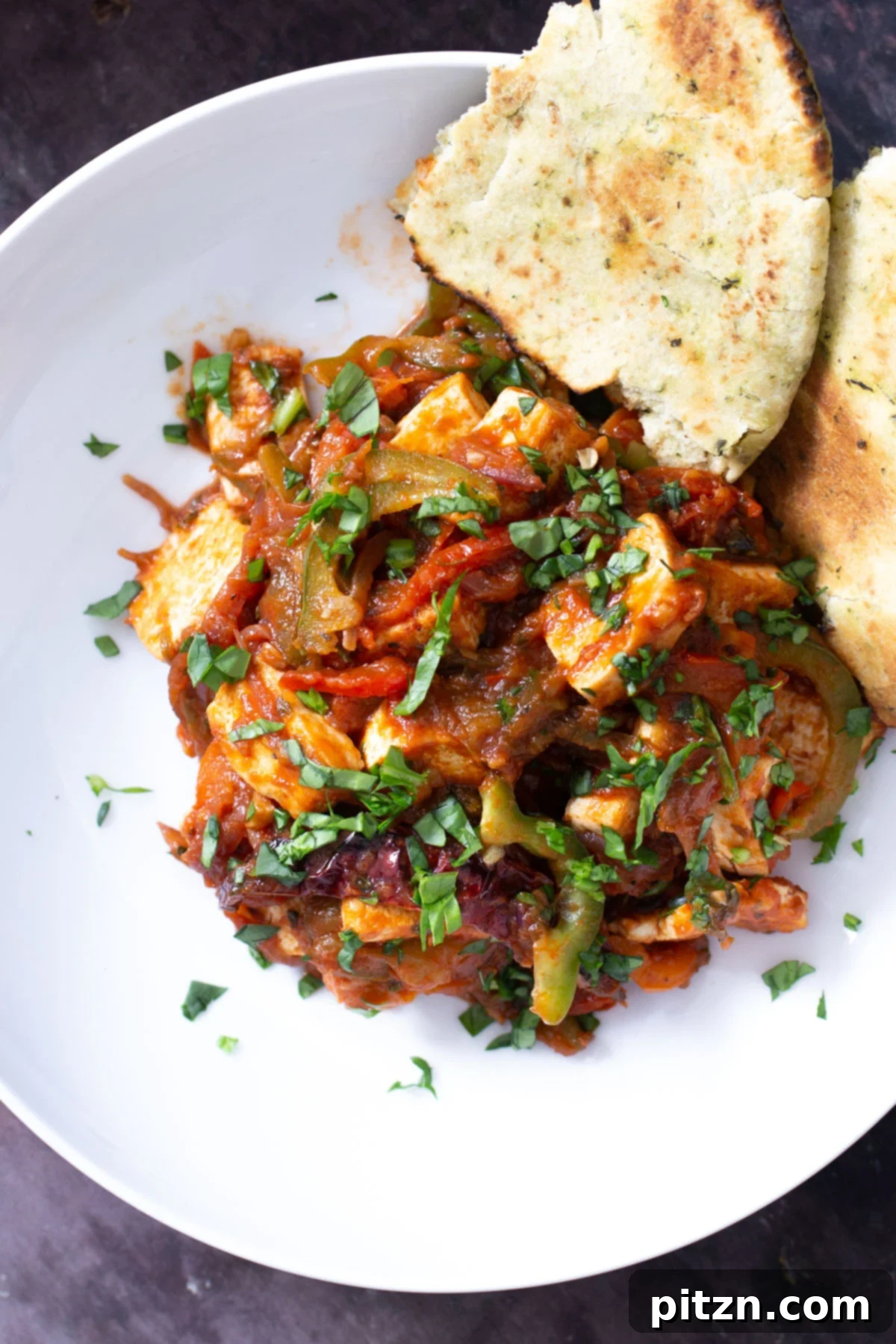 A beautifully arranged serving of Tofu Jalfrezi curry in a white bowl, accompanied by a side of warm naan bread and fresh cilantro garnish.