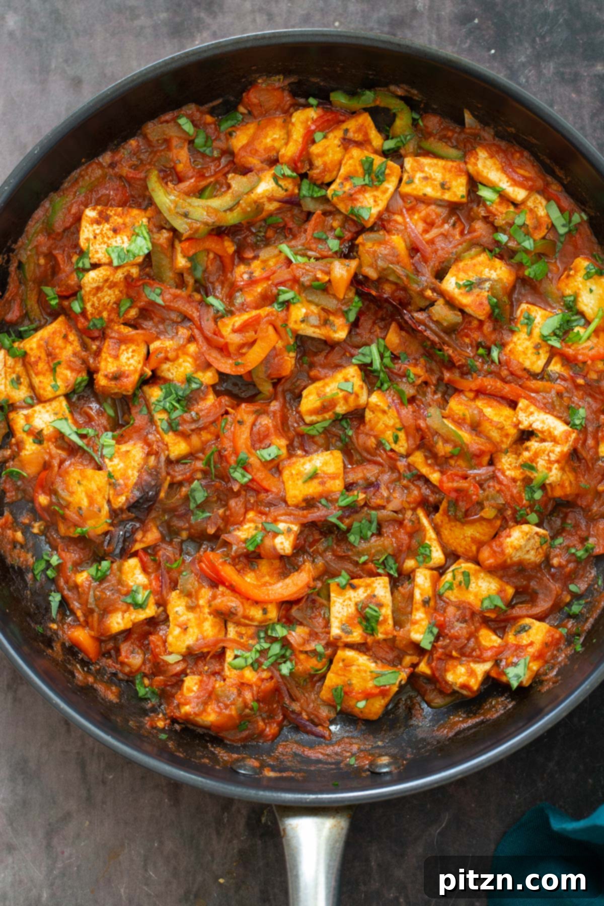 A black skillet filled with simmering Vegan Tofu Jalfrezi sauce, featuring golden tofu cubes and bell peppers, garnished with fresh cilantro.