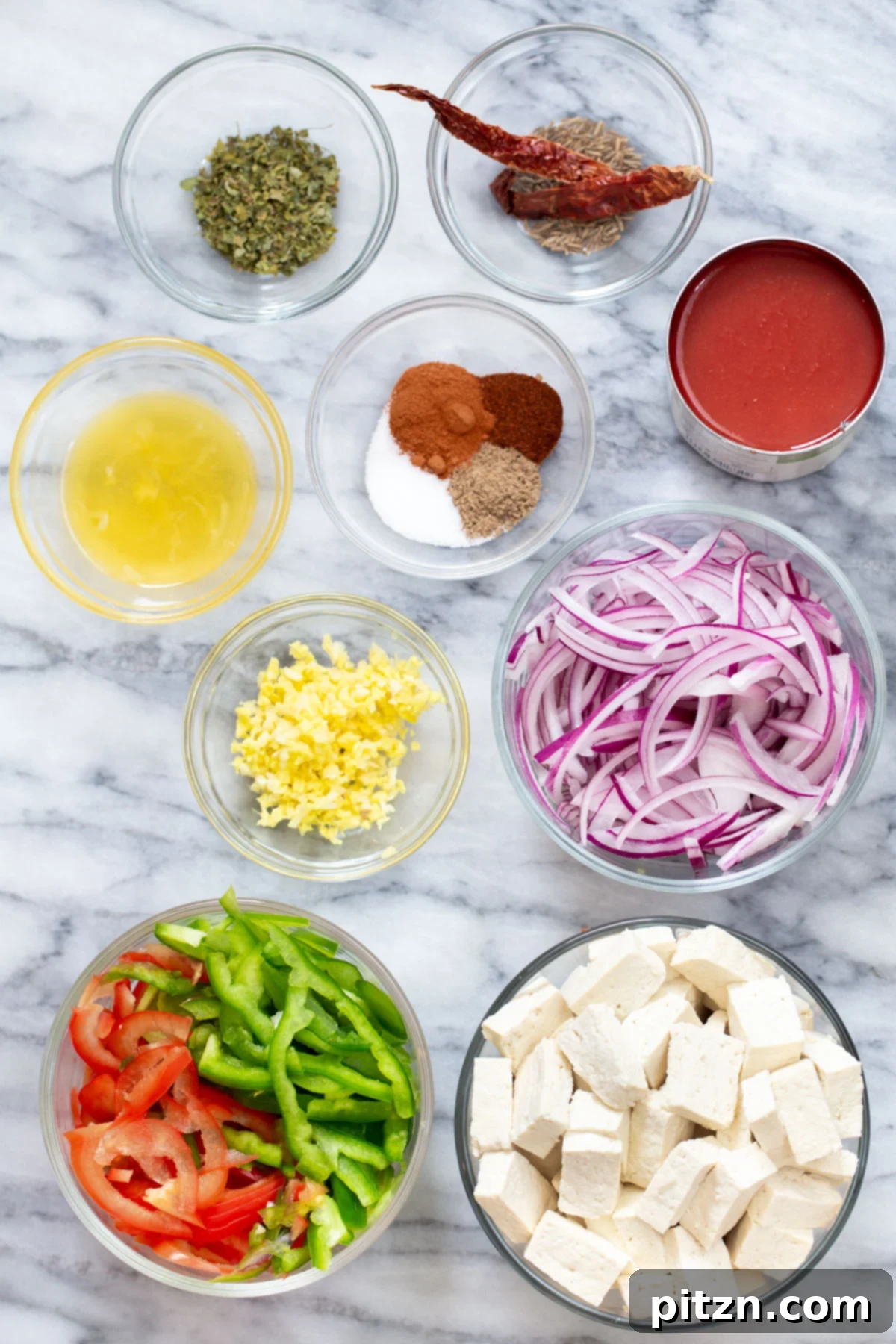 A vibrant display of fresh ingredients for Vegan Jalfrezi Tofu Curry, including bell peppers, onions, ginger, garlic, tofu, and various spices.