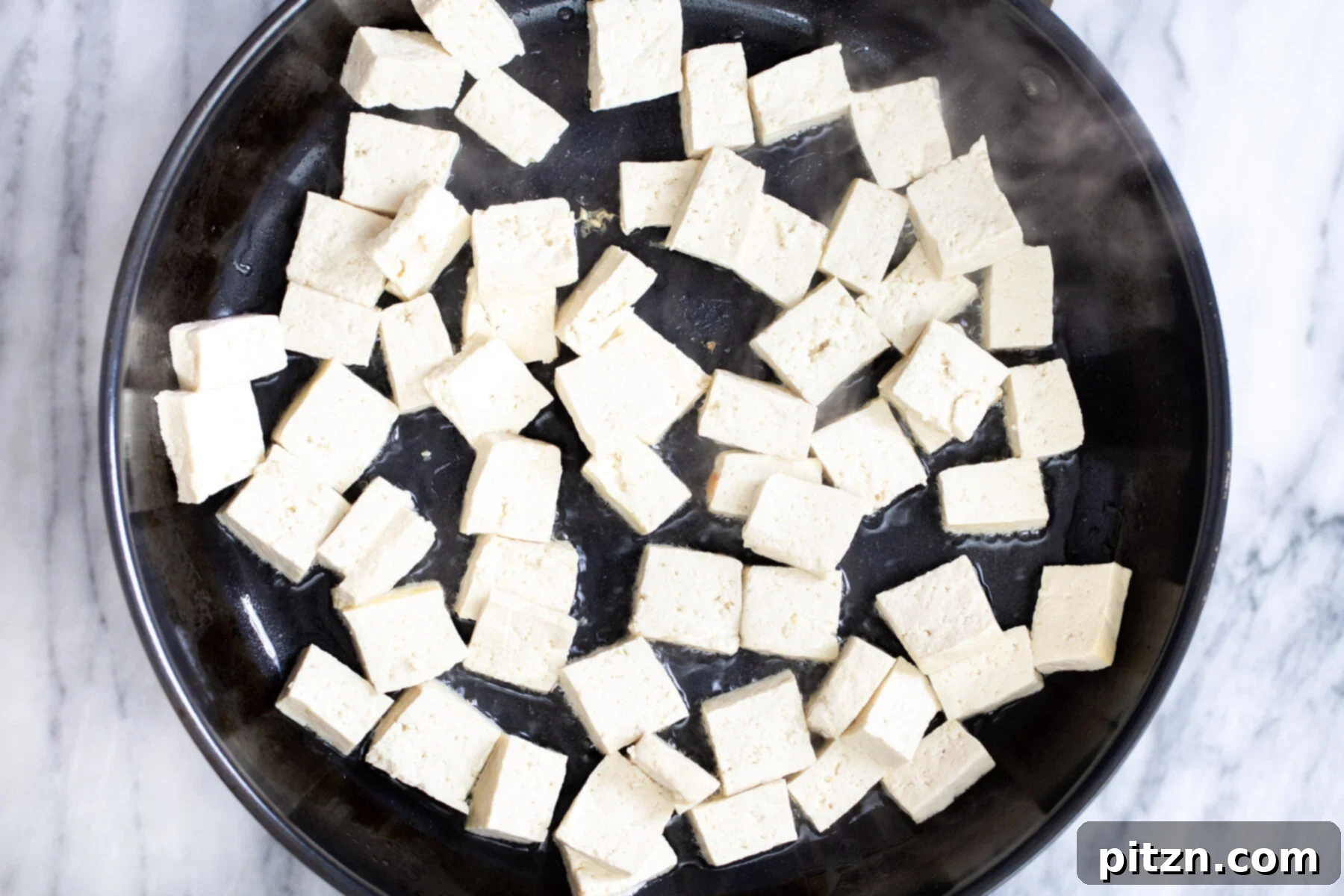 Pressed tofu cubes in a frying pan, ready to be seared for Vegan Tofu Jalfrezi.