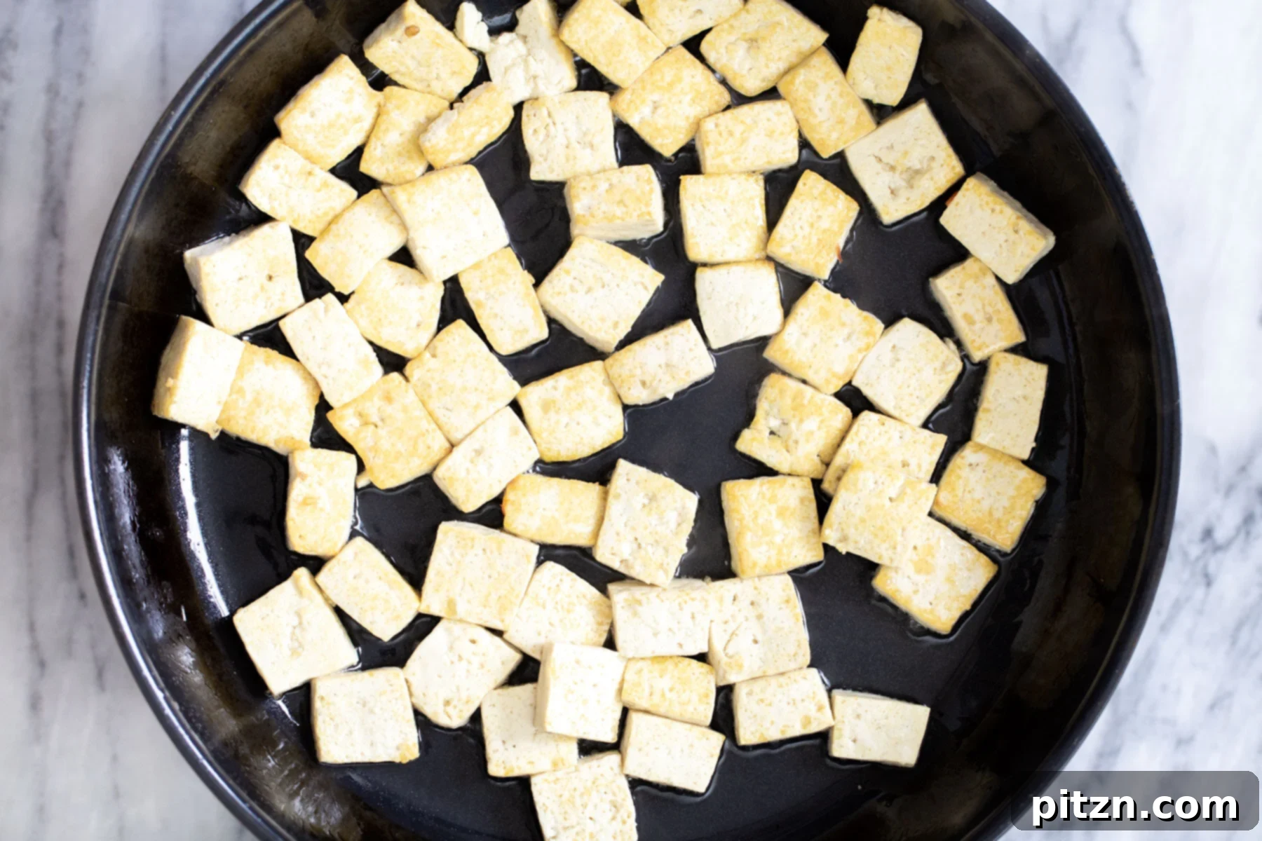 Golden seared tofu cubes in a frying pan, removed from the skillet after achieving a perfect crust.