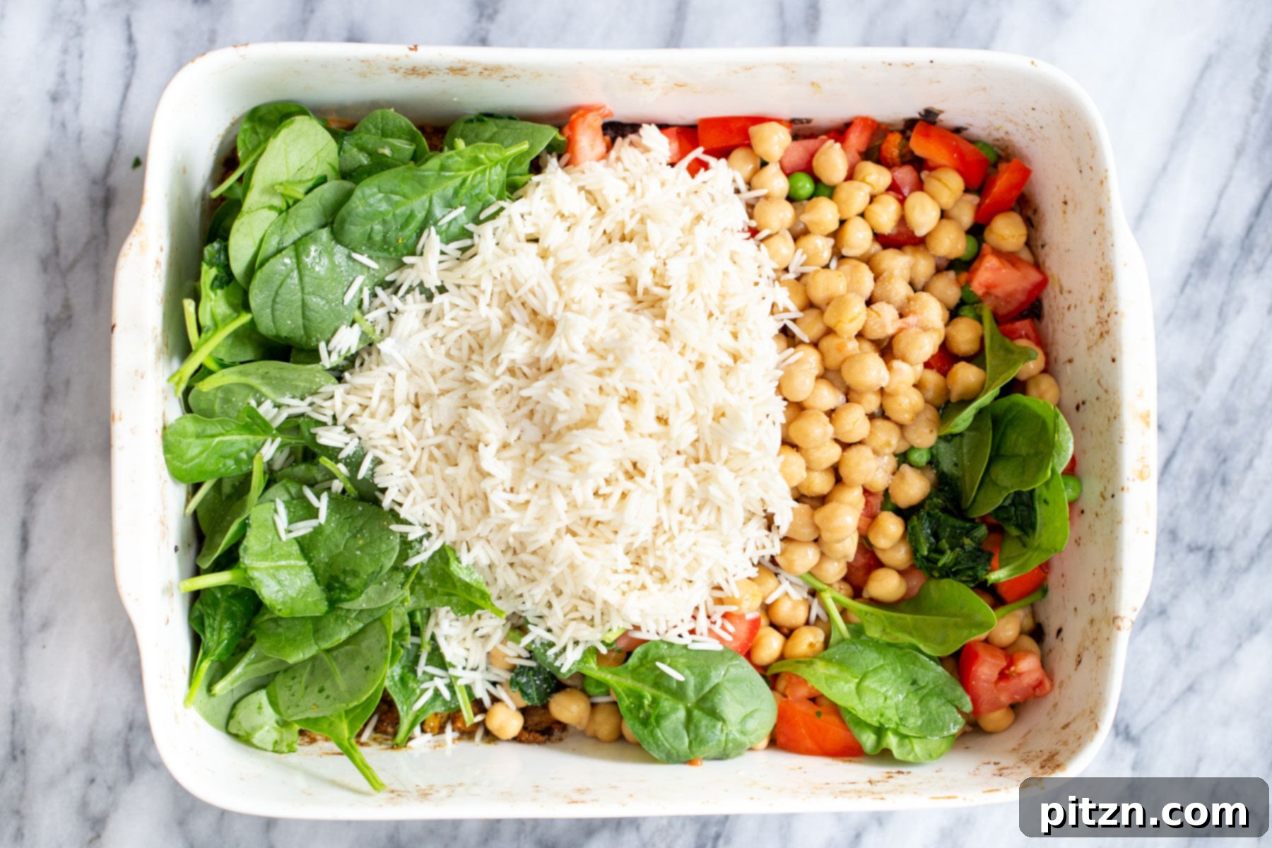 Golden Spiced Vegan Chickpea Rice Bake 10 Soaked rice, tender chickpeas, and fresh spinach being incorporated into the roasted vegetables in a white casserole dish.
