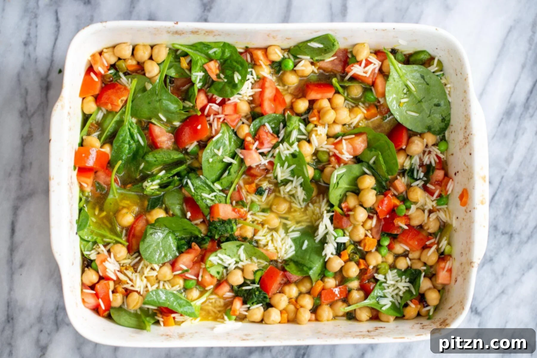 Golden Spiced Vegan Chickpea Rice Bake 11 A close-up of spinach, tomatoes, chickpeas, and drained, soaked rice evenly spread in a casserole dish, ready for the final bake.