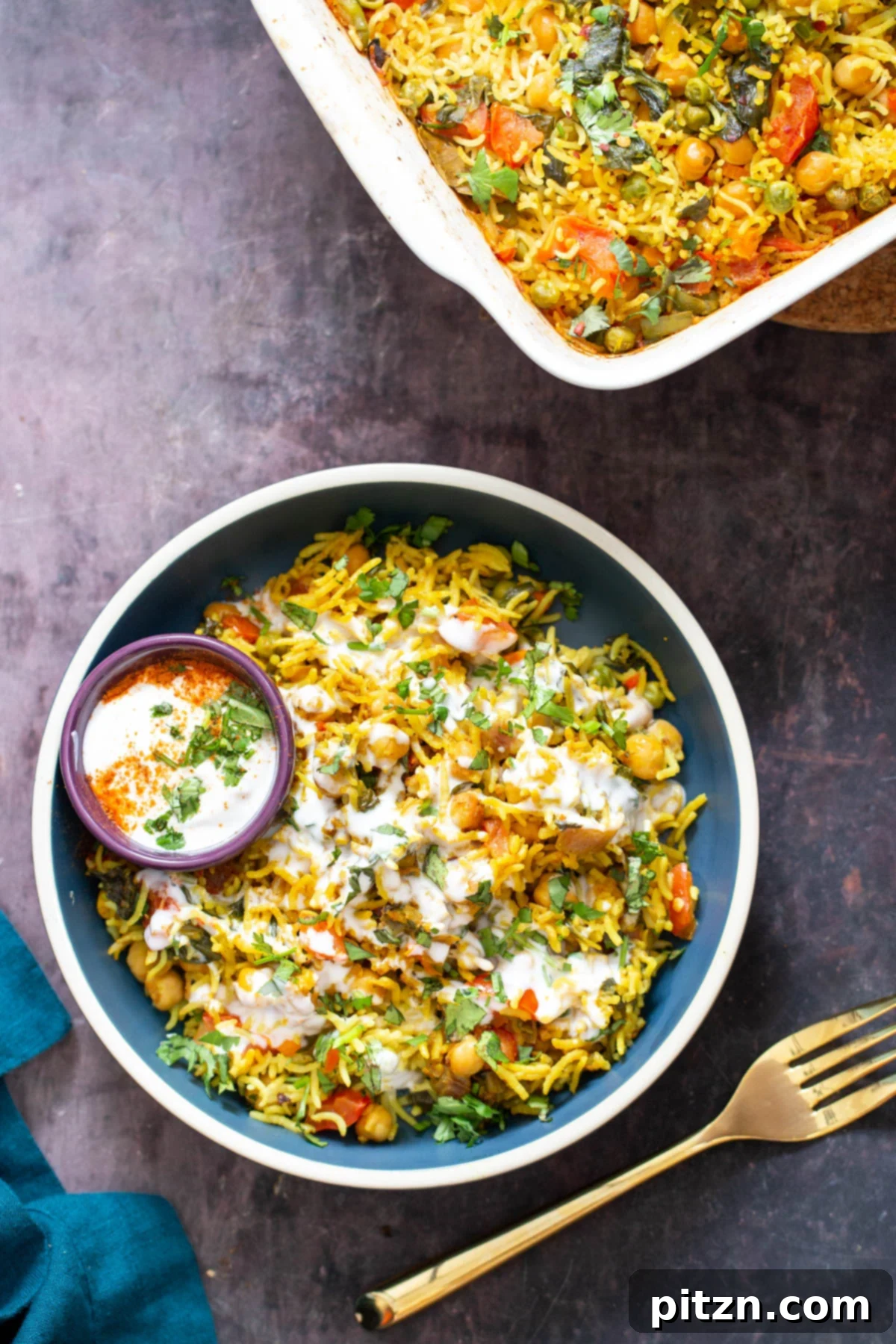 Golden Spiced Vegan Chickpea Rice Bake 3 A small blue bowl of vegan chana pulao chickpea rice casserole, elegantly drizzled with raita, capturing a moment of culinary delight.