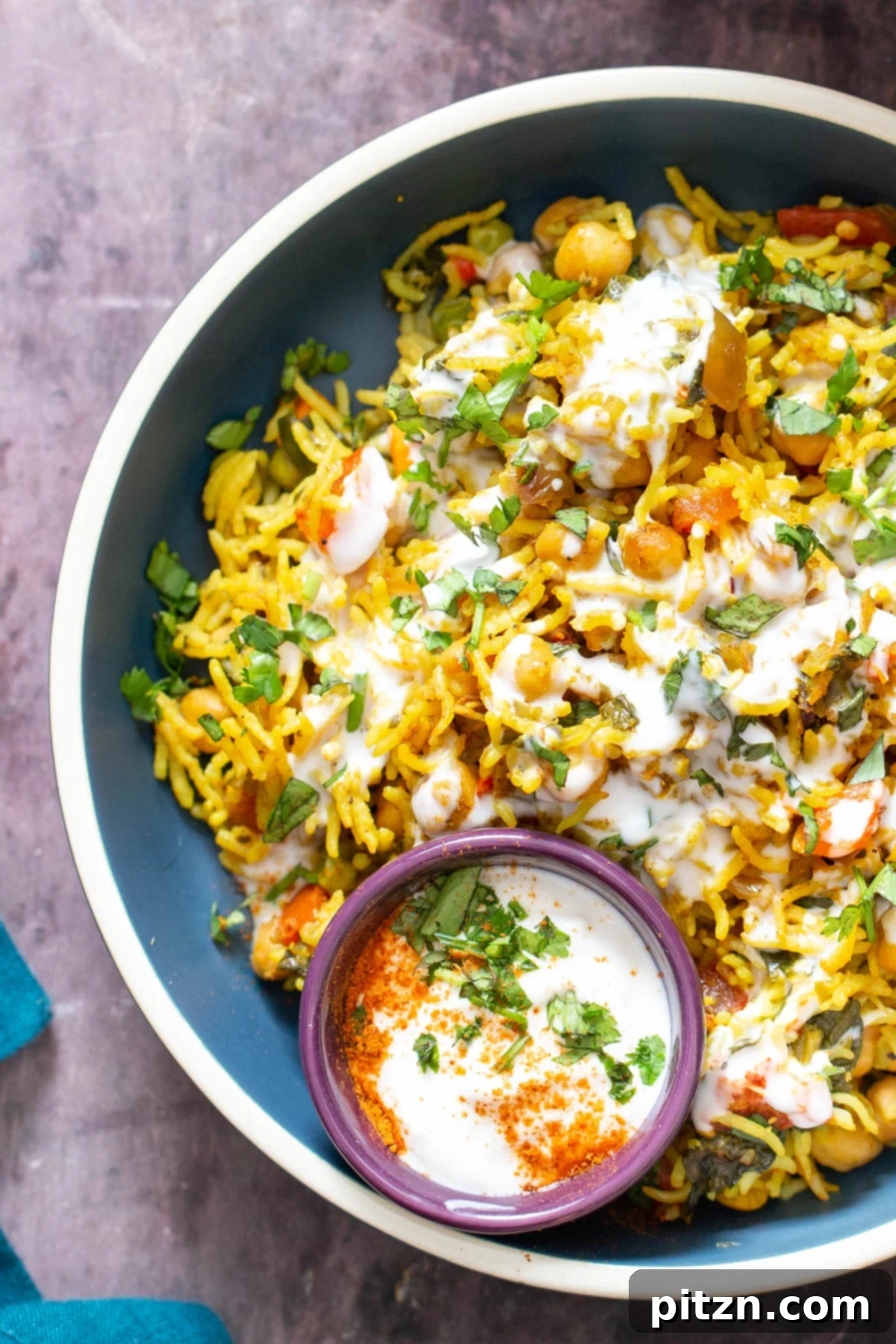 A beautifully presented bowl of baked vegan chickpea pulao, generously drizzled with cool raita, enhancing its visual appeal.