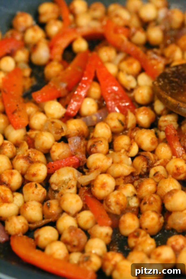 Chickpeas with blackening spice being added to vegetables in a pan