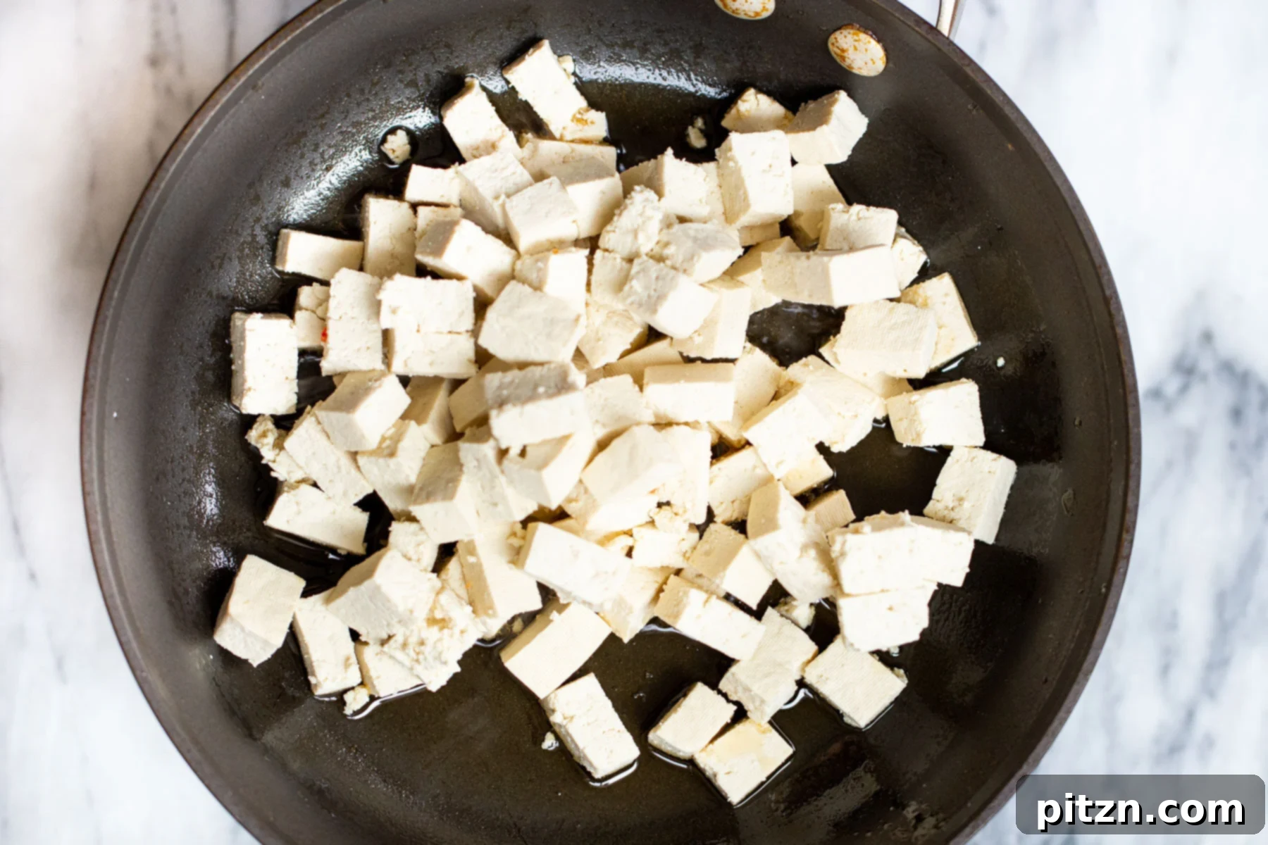 tofu cubes frying in a black skillet 