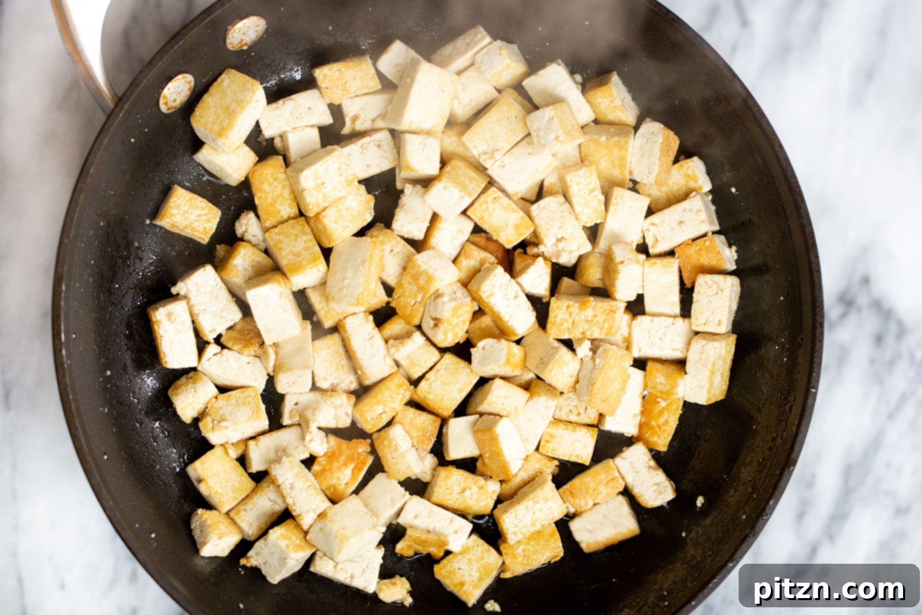 tofu cubes being fried in a black skillet 