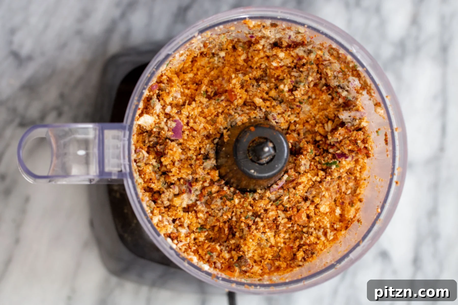A small food processor filled with the completed cauliflower taco meat mixture, showcasing its fine, crumbly texture.