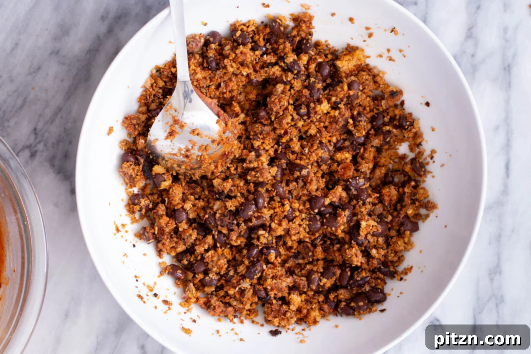 A small dish showing cauliflower taco meat being combined with black beans and green chilies, beginning the filling assembly.
