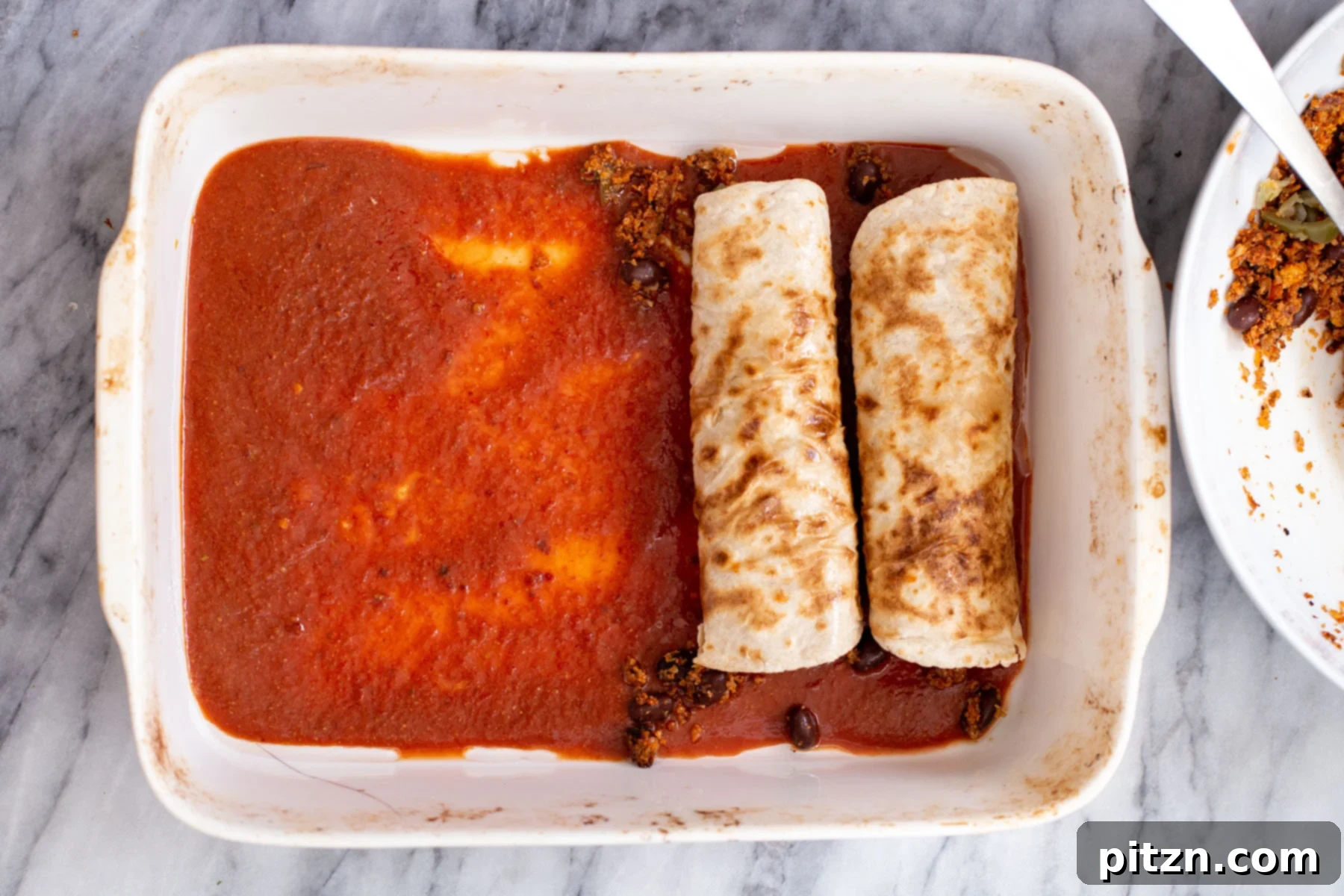 Hands filling and rolling tortillas with vegan cauliflower taco meat and placing them neatly into a casserole dish.