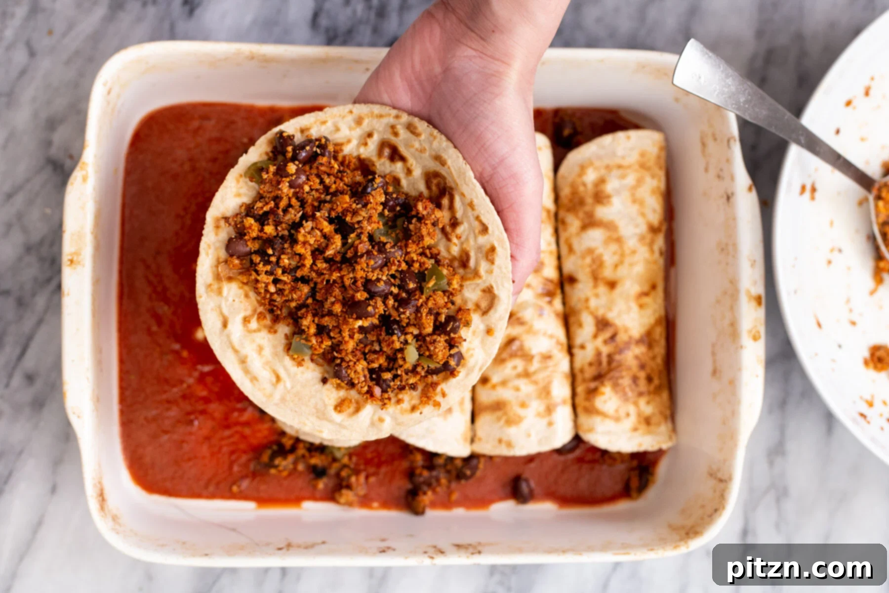A hand holding a whole wheat tortilla generously filled with savory vegan cauliflower taco meat, ready to be rolled.