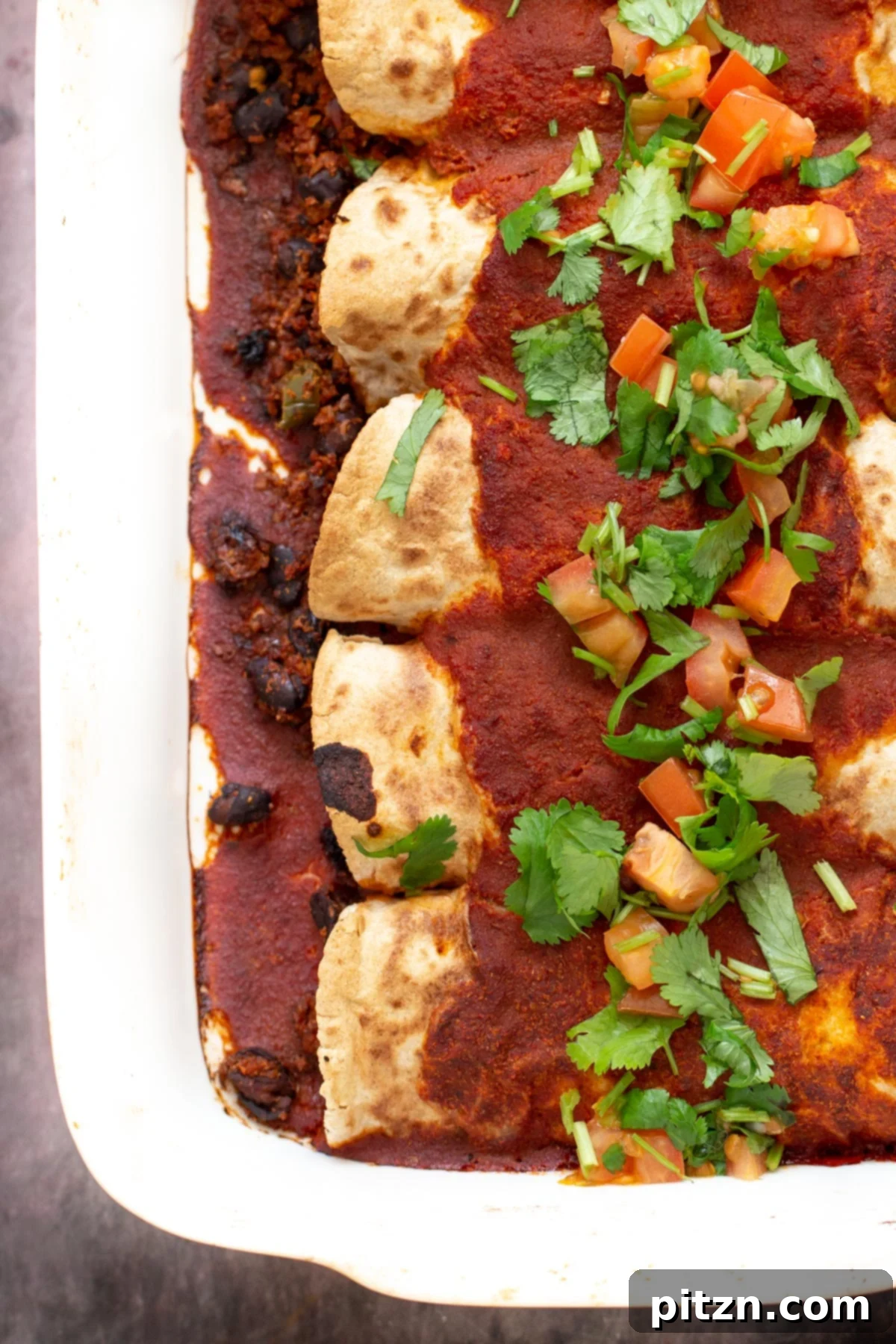 A casserole dish brimming with hearty vegan enchiladas, generously covered in a vibrant tomato sauce and garnished with fresh cilantro.