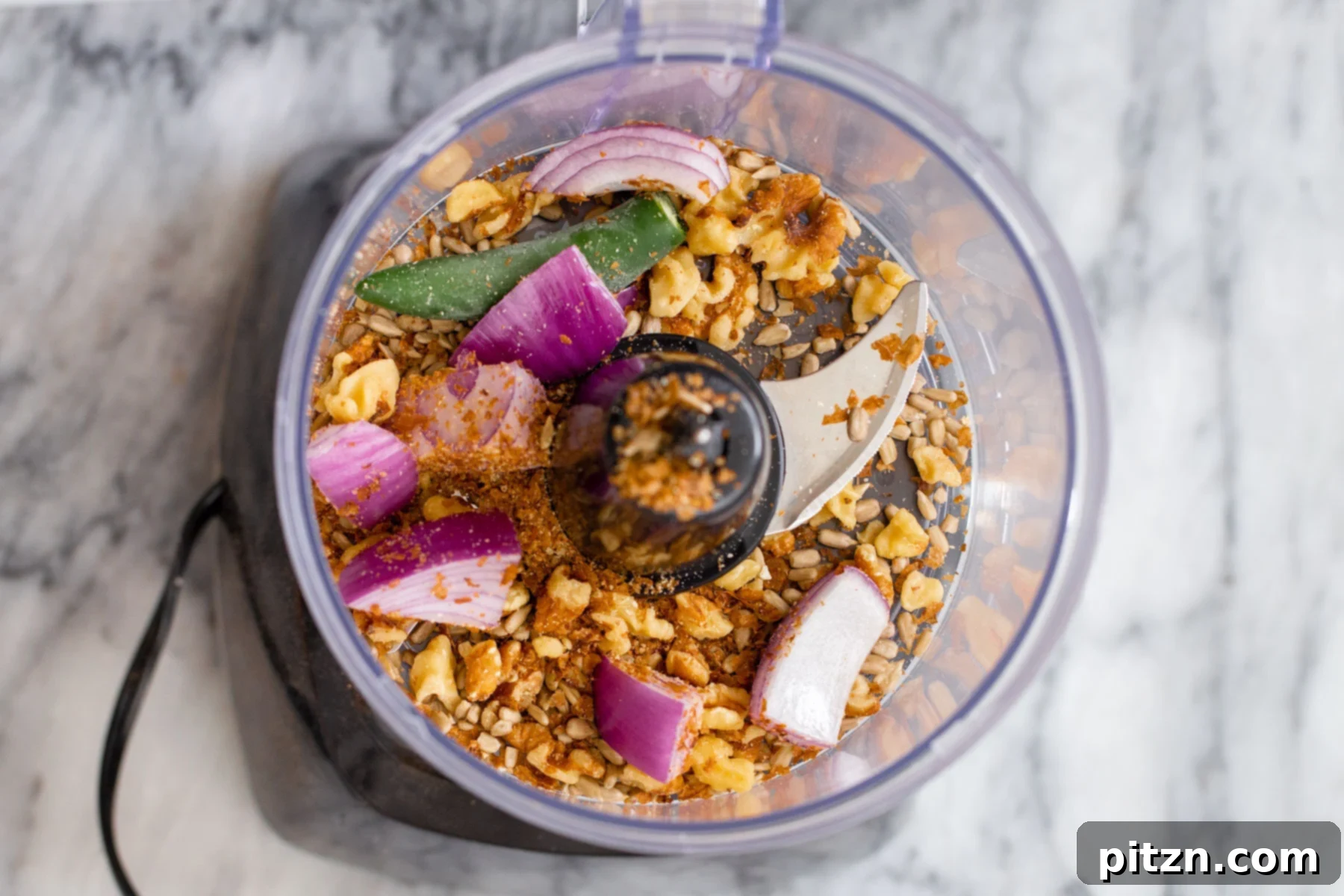 A food processor bowl filled with the initial ingredients for vegan cauliflower taco meat: walnuts, onion, and jalapeño, ready for blending.