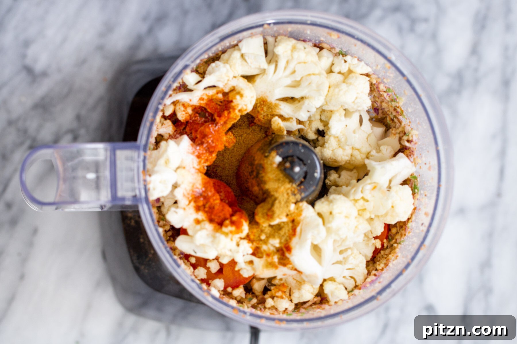 More cauliflower and taco meat seasoning ingredients added to a small food processor for the next stage of blending.