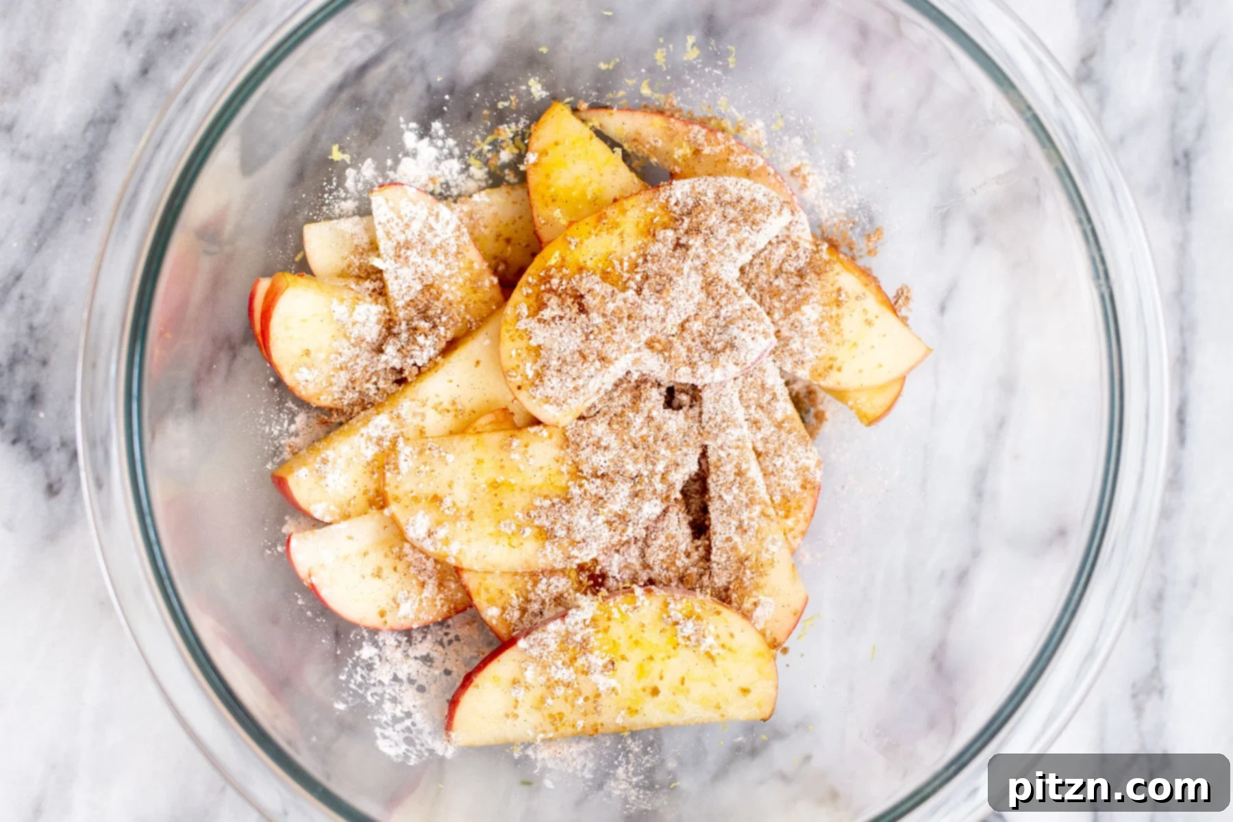 apple slices in a glass bowl being mixed with brown sugar and cornstarch