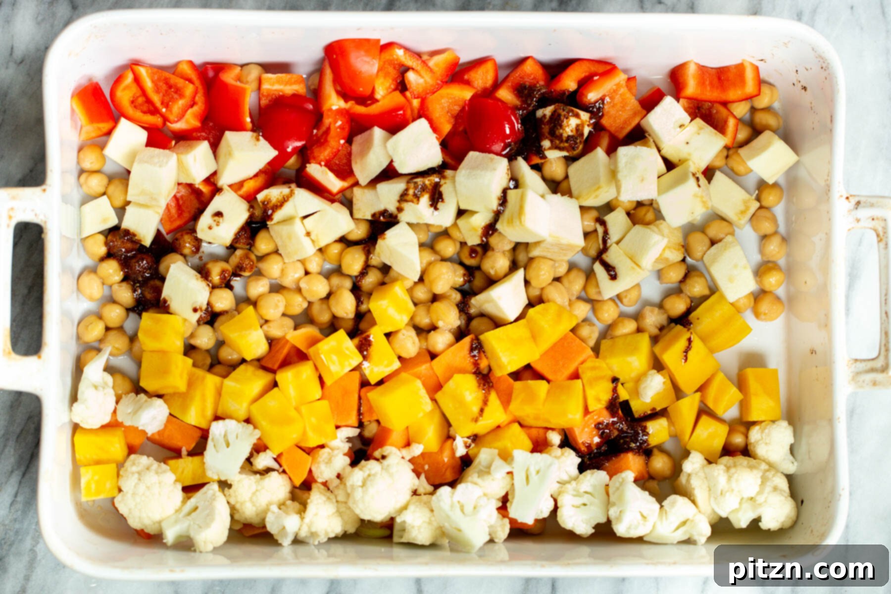 maple syrup and balsamic vinegar being drizzled over chopped veggies in casserole dish