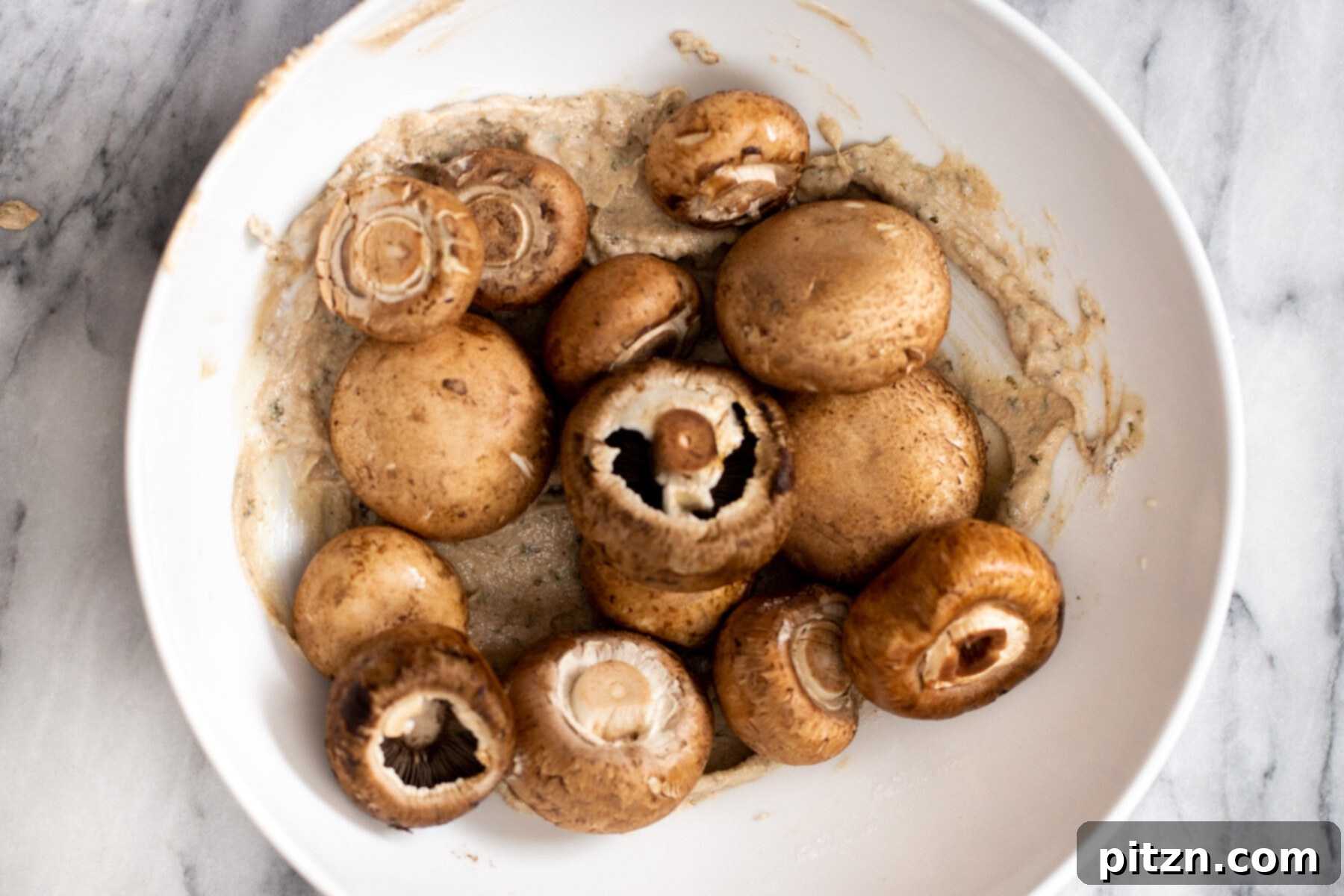 Swedish Plant-Ball Perfection 10 Whole cremini mushrooms being expertly tossed with the creamy marinade in a white mixing bowl.
