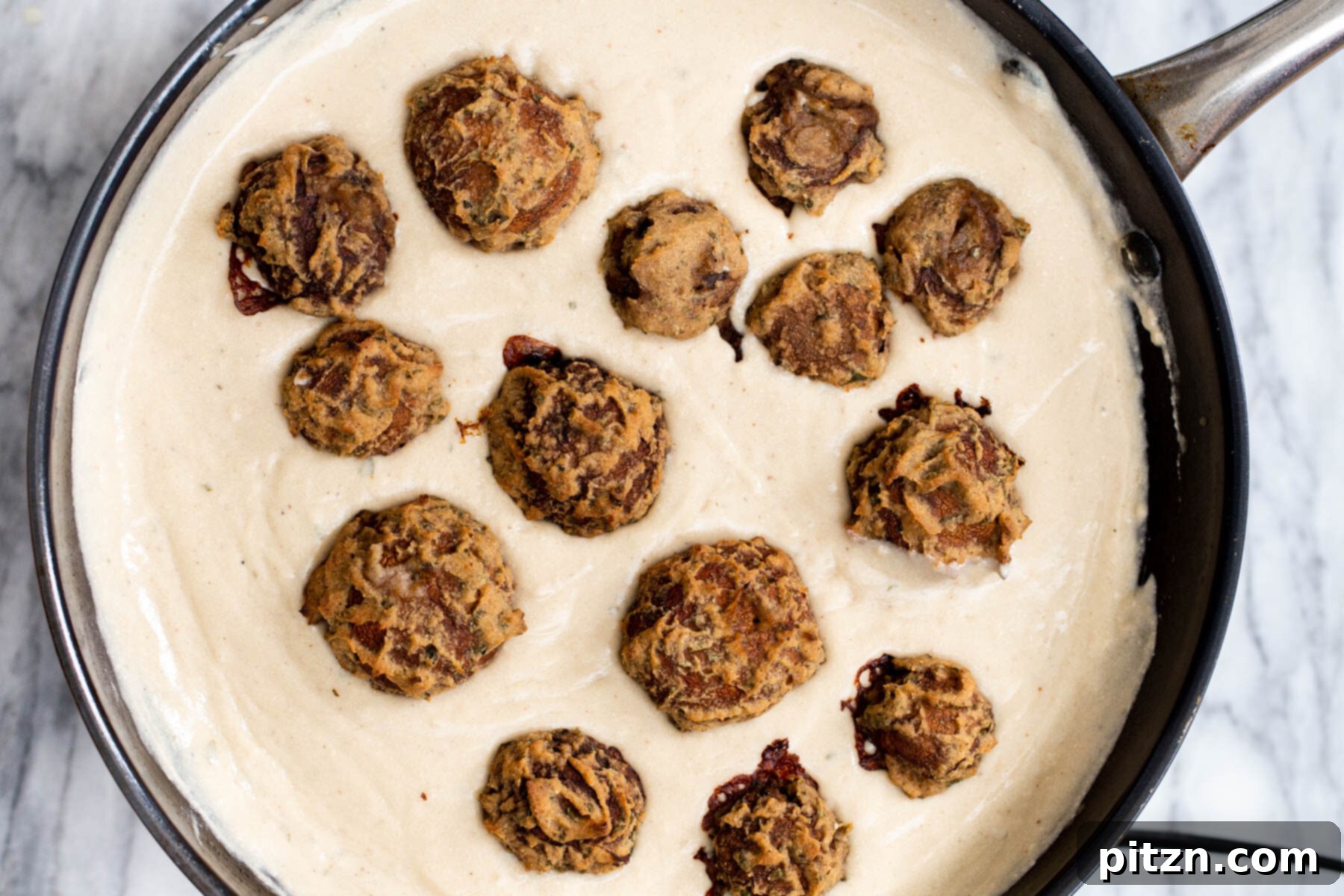 Swedish Plant-Ball Perfection 20 Baked vegan mushroom balls being carefully placed into a saucepan filled with creamy gravy.