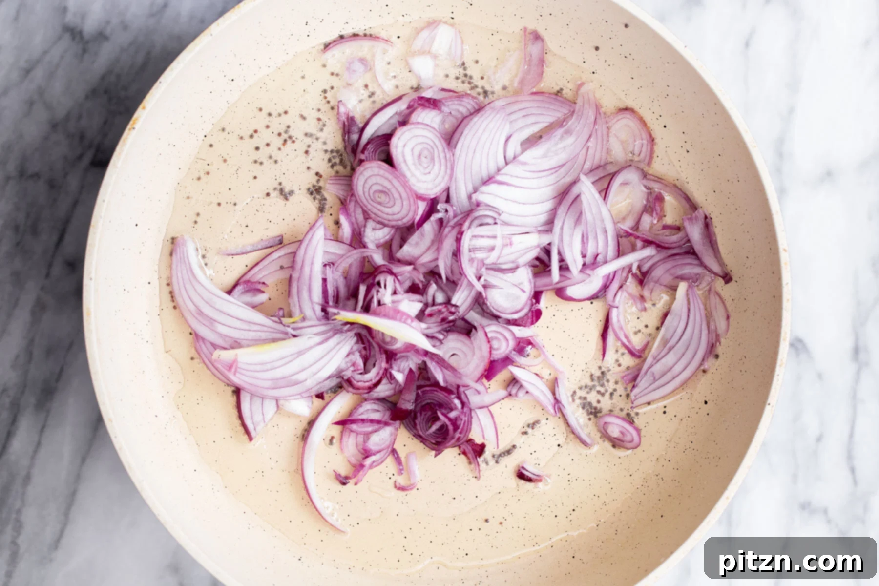 Thinly sliced red onions being carefully added to a frying pan, joining the sizzling mustard seeds, to begin the sautéing process.