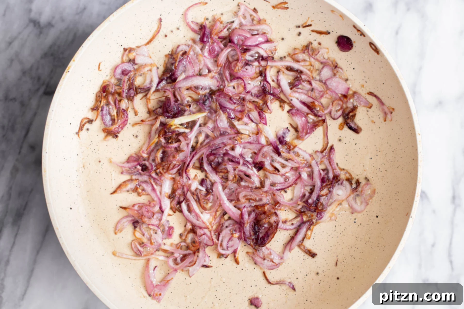 A close-up view of perfectly golden-brown sautéed onions within a white pan, exuding a fragrant and sweet aroma.