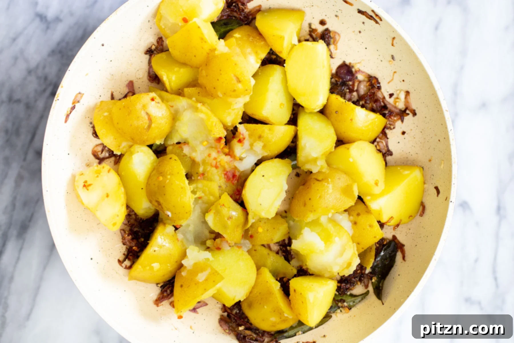 Tender boiled potatoes being introduced into the sautéing pan, mixing with the flavorful fried onions and aromatic tempering.
