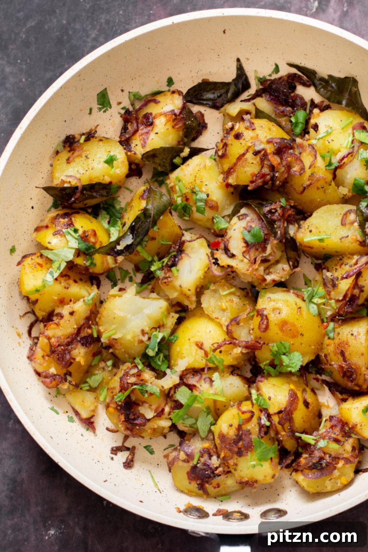 A close-up shot of crispy, golden-brown potatoes in a frying pan, generously seasoned with spices and fresh cilantro.