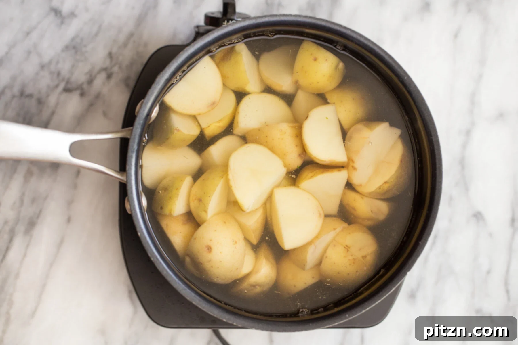 Potatoes boiling vigorously in a saucepan with turmeric, salt, and pepper flakes, imparting a rich yellow color to the water.