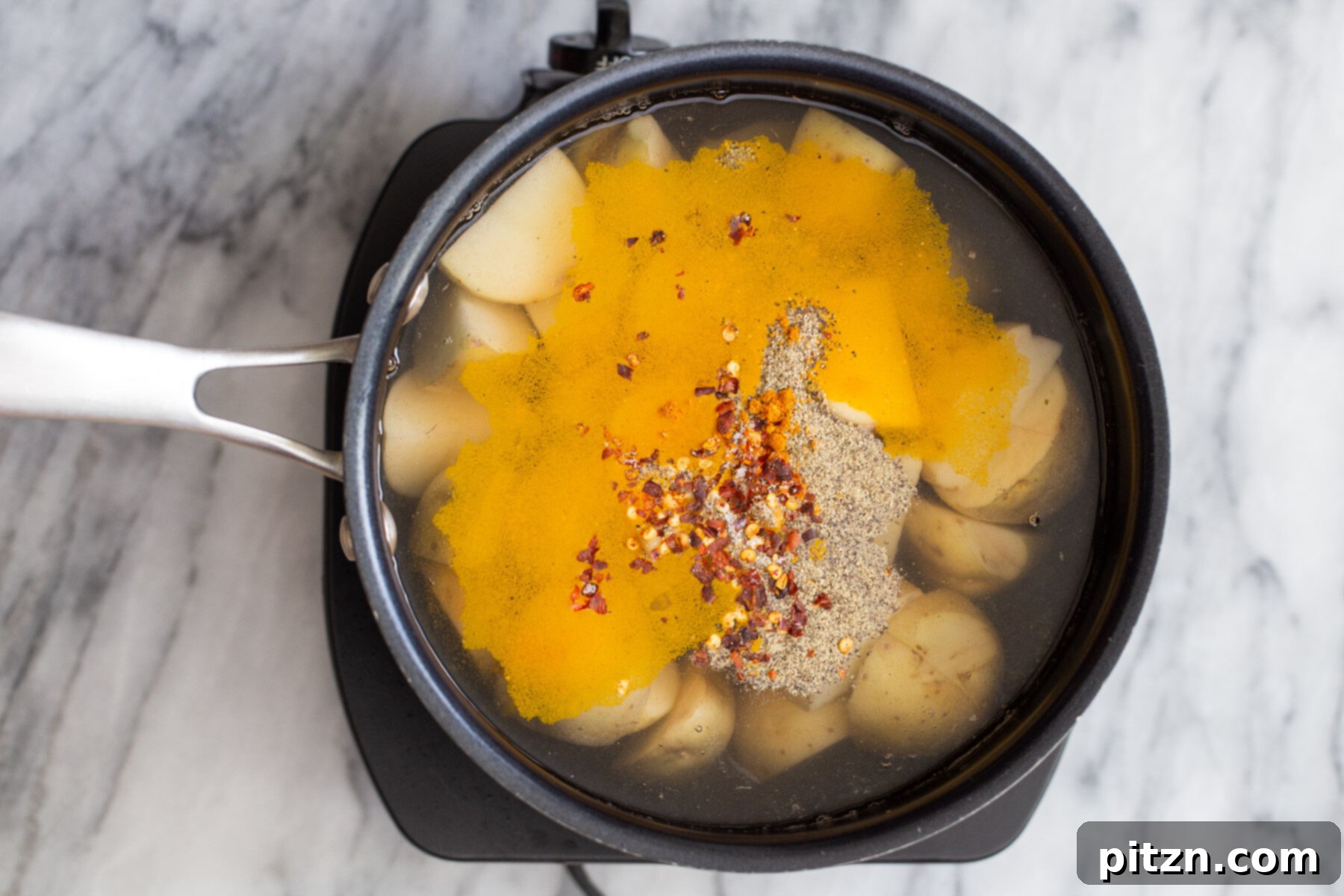 A close-up view of turmeric, black pepper, and red pepper flakes being carefully added into a pot of water, preparing for potato boiling.