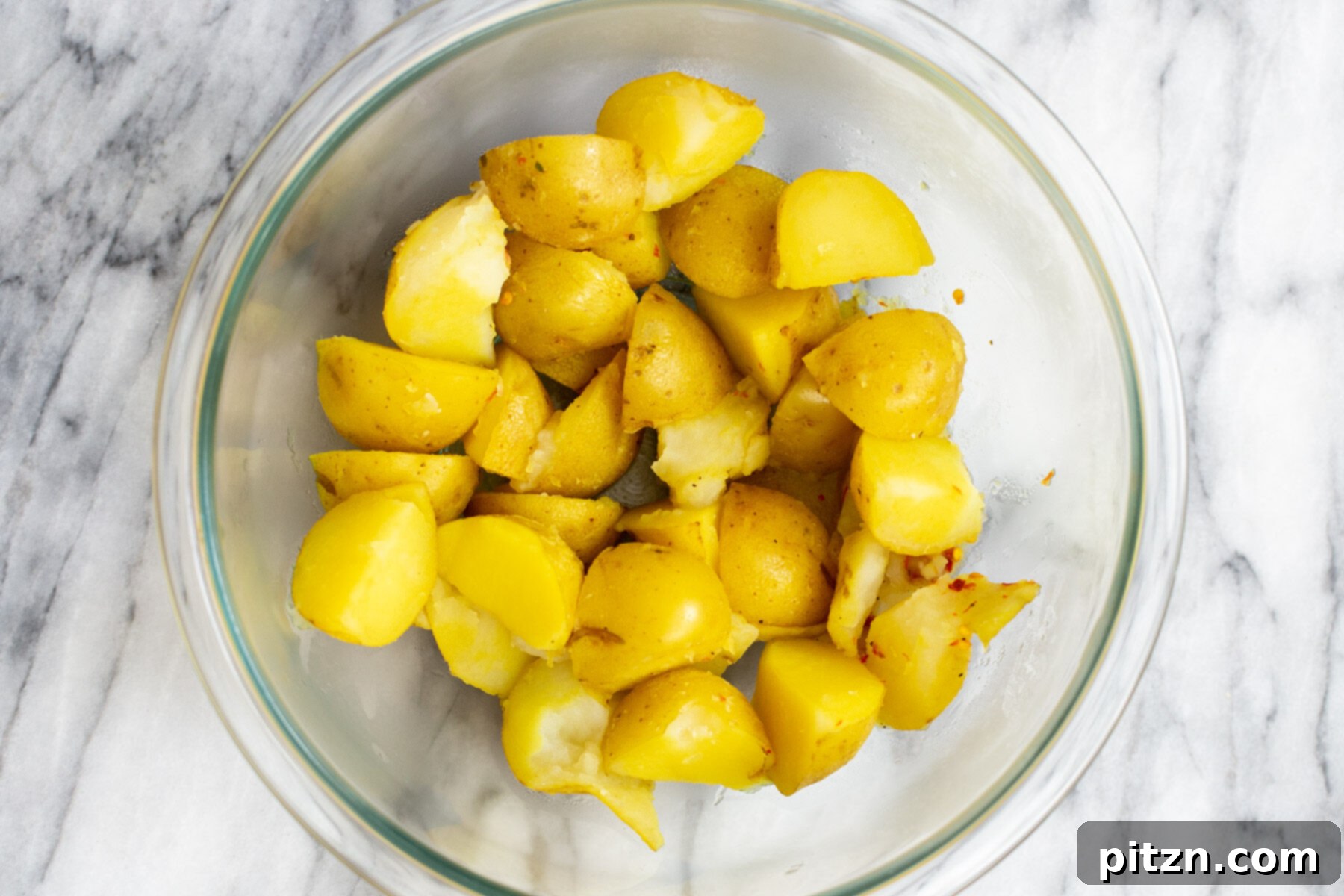 A clear glass bowl filled with perfectly boiled potatoes, seasoned and ready for the next stages of stir-frying.