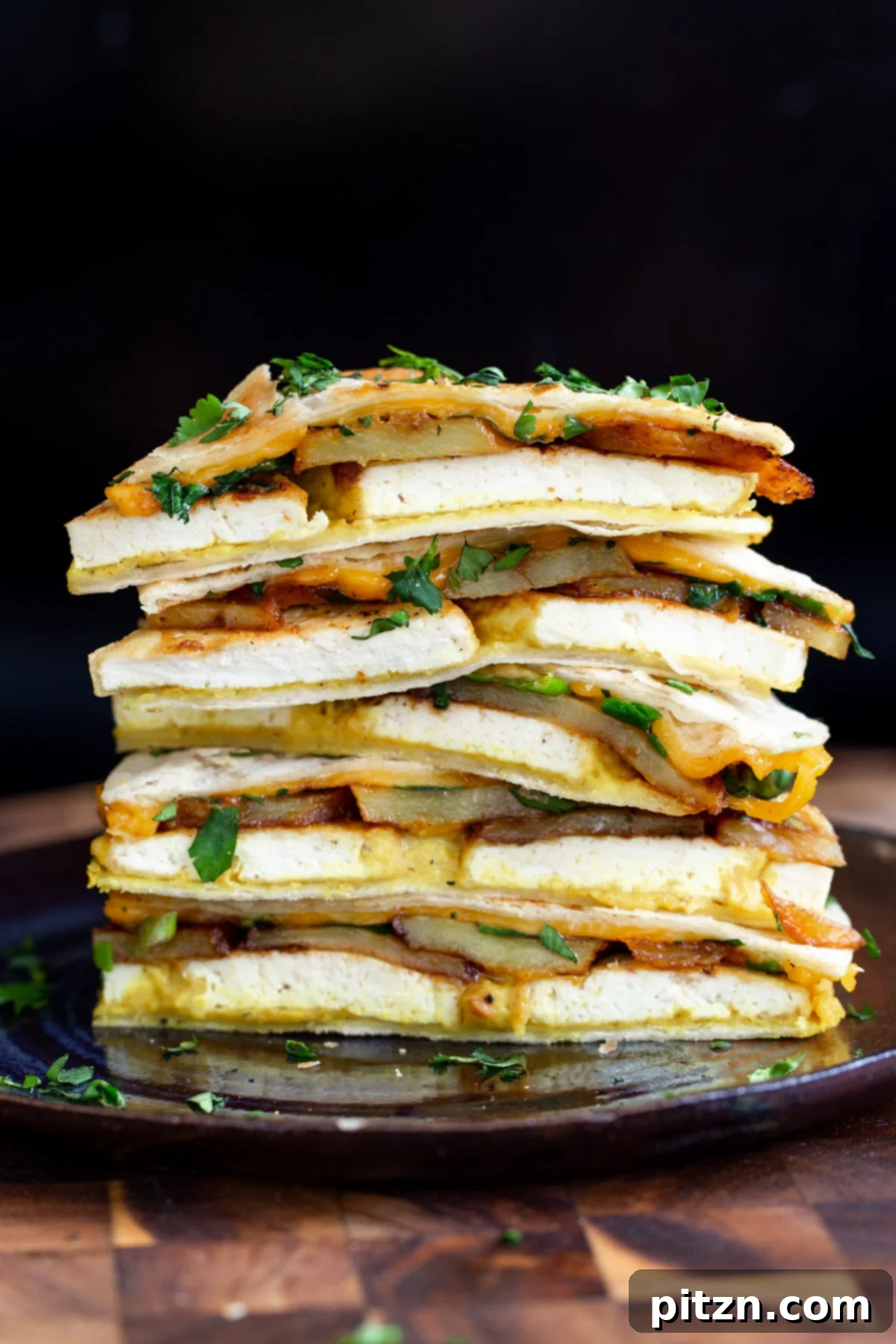 Smoky Tofu and Potato Sunrise Quesadillas 3 Stacked wedges of vegan breakfast quesadilla with potatoes and tofu, garnished with fresh cilantro.
