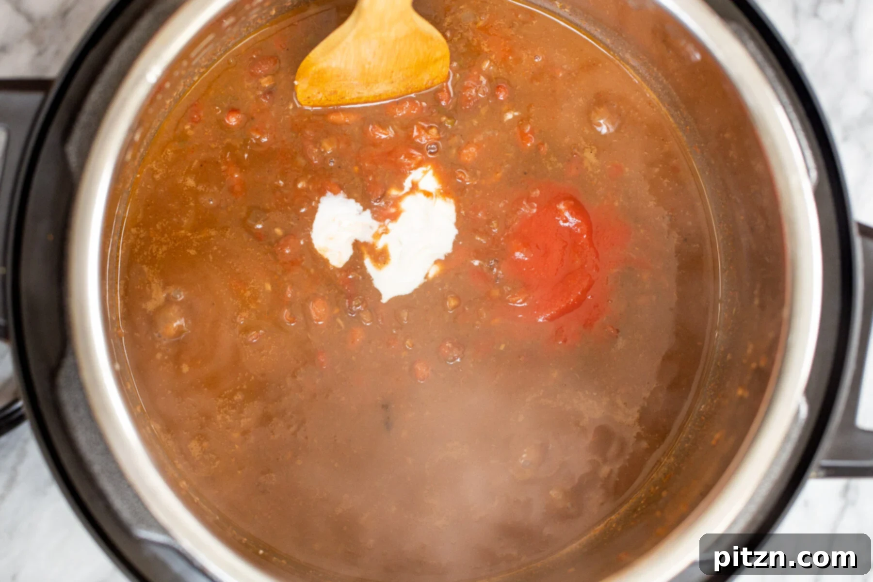 Instant Pot Dhaba Rajma: Authentic & Easy Kidney Bean Curry 12 dairy-free yogurt and rich tomato paste being skillfully stirred into the creamy kidney bean curry in an Instant Pot