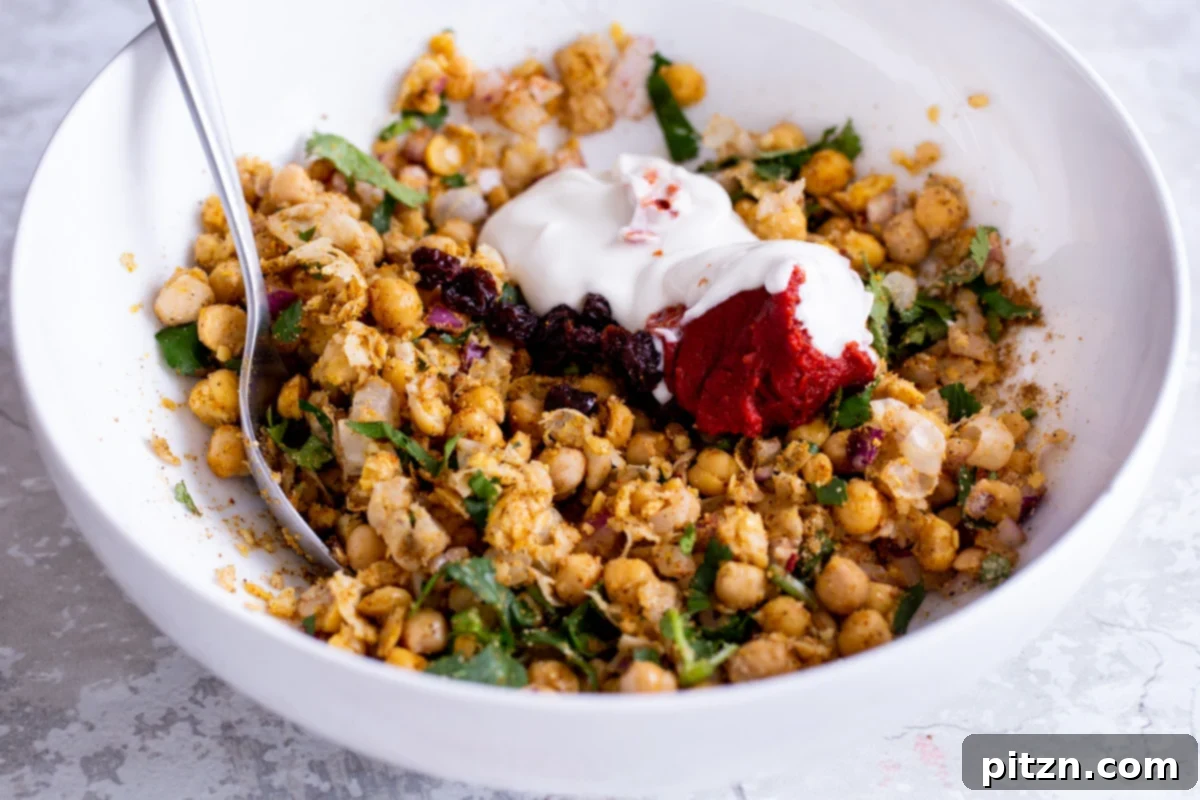 Plant-based yogurt being stirred into mashed chickpeas and herbs in a white bowl, creating a creamy texture
