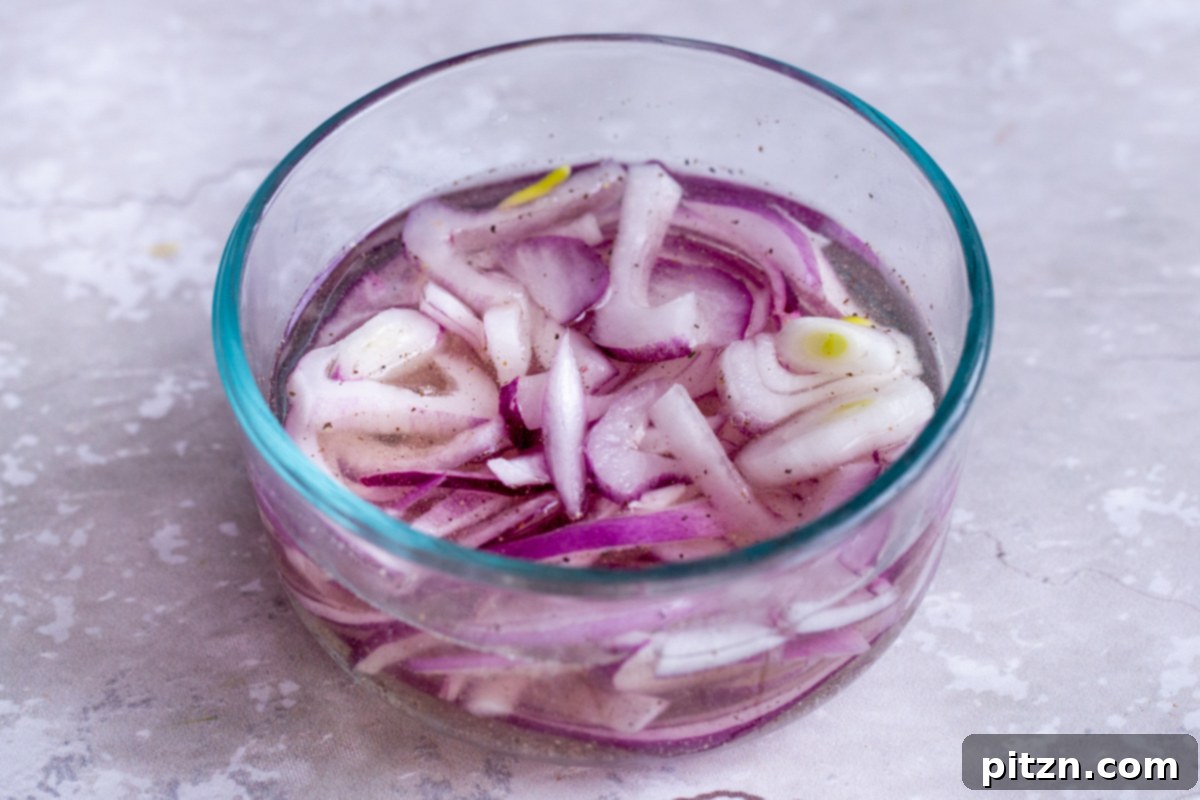 Thinly sliced red onions being carefully added to a small bowl of pickling brine
