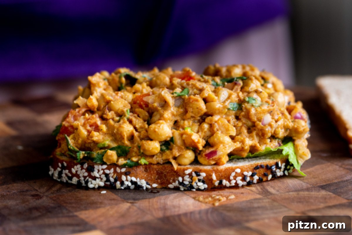 Creamy curried chickpea salad being spread generously onto a slice of bread, ready for assembly