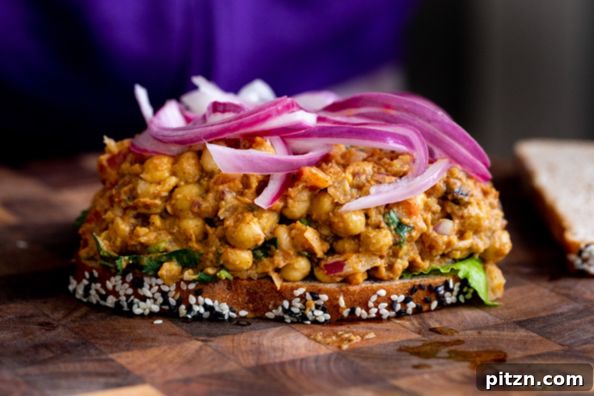 A slice of bread topped with curried chickpea salad and vibrant quick pickled red onions, ready for the top bread slice