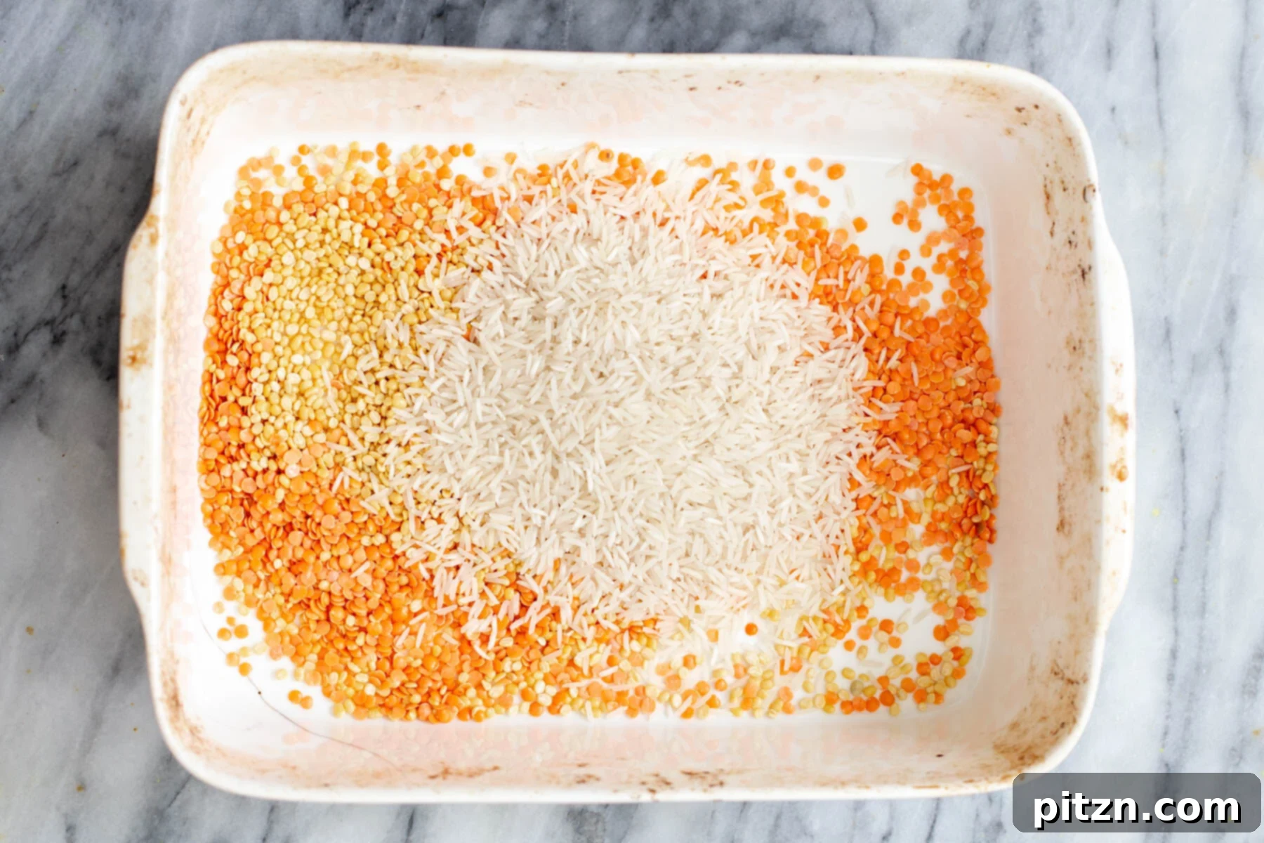 Spiced Kitchari Comfort Bake 8 Uncooked lentils and rice being gently poured into a casserole dish, marking the initial step in preparing the Baked Kitchari Casserole.