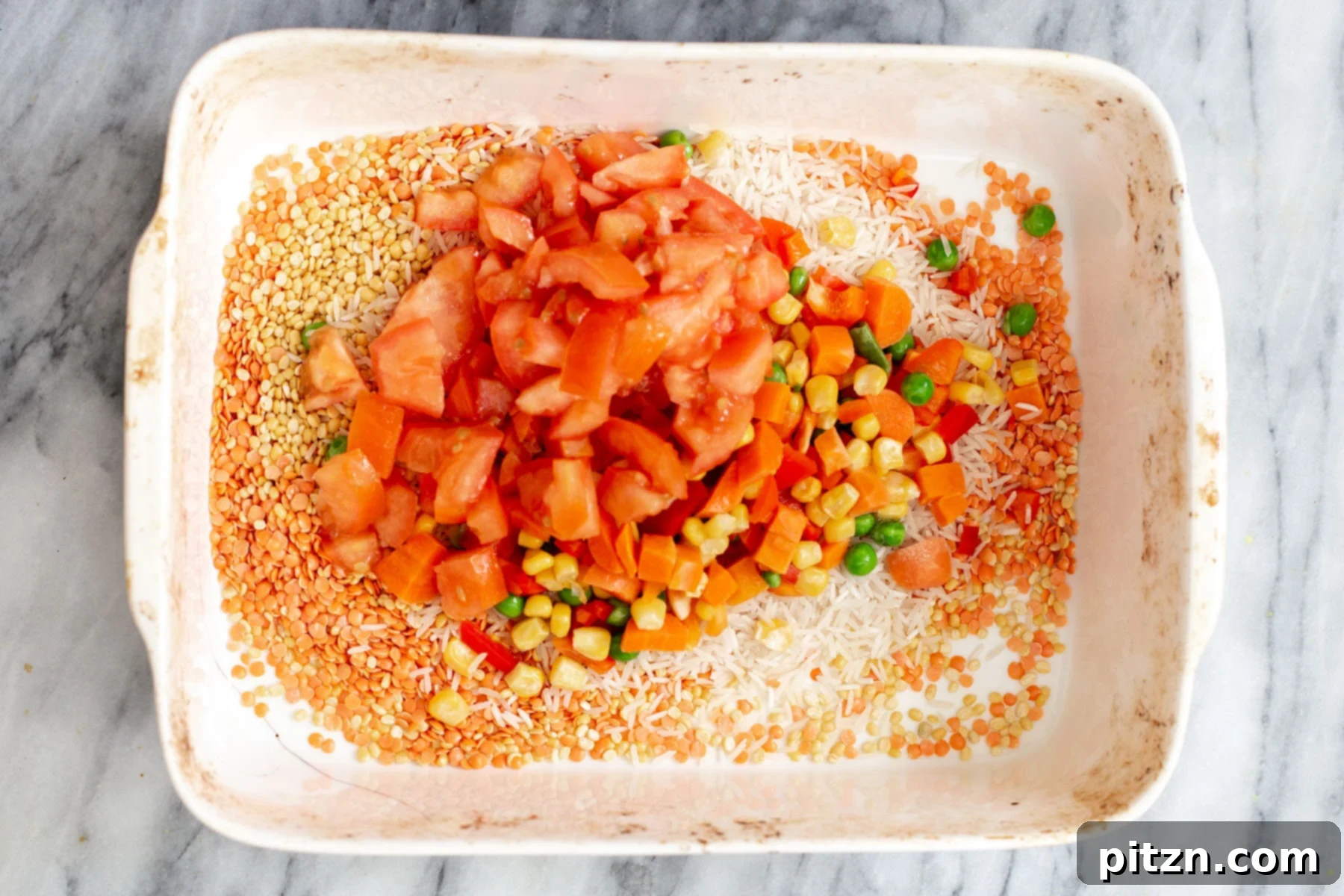 Spiced Kitchari Comfort Bake 9 Vibrant fresh tomatoes and an assortment of vegetables being added to a casserole dish containing rice and red lentils, creating a colorful and healthy base for the Kitchari casserole.