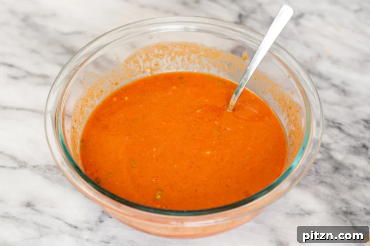 A small, clear glass dish filled with the vibrant, orange-hued Tikka Masala sauce, now fully blended and ready for use. Its creamy texture and rich color are enticing, inviting a delicious dipping experience.