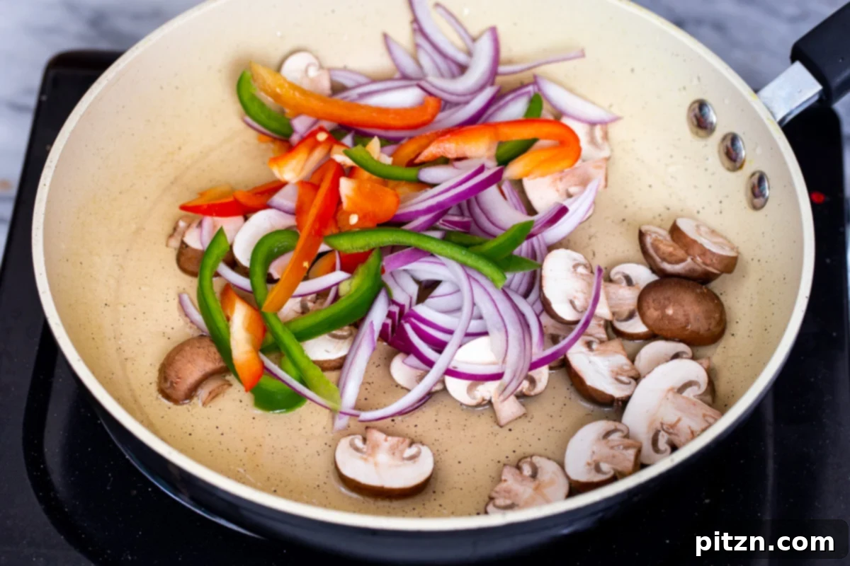 Thinly sliced mushrooms, green bell peppers, red bell peppers, and red onions are being added to a hot skillet, beginning the sautéing process for the vegan birria taco filling. Steam gently rises from the pan.